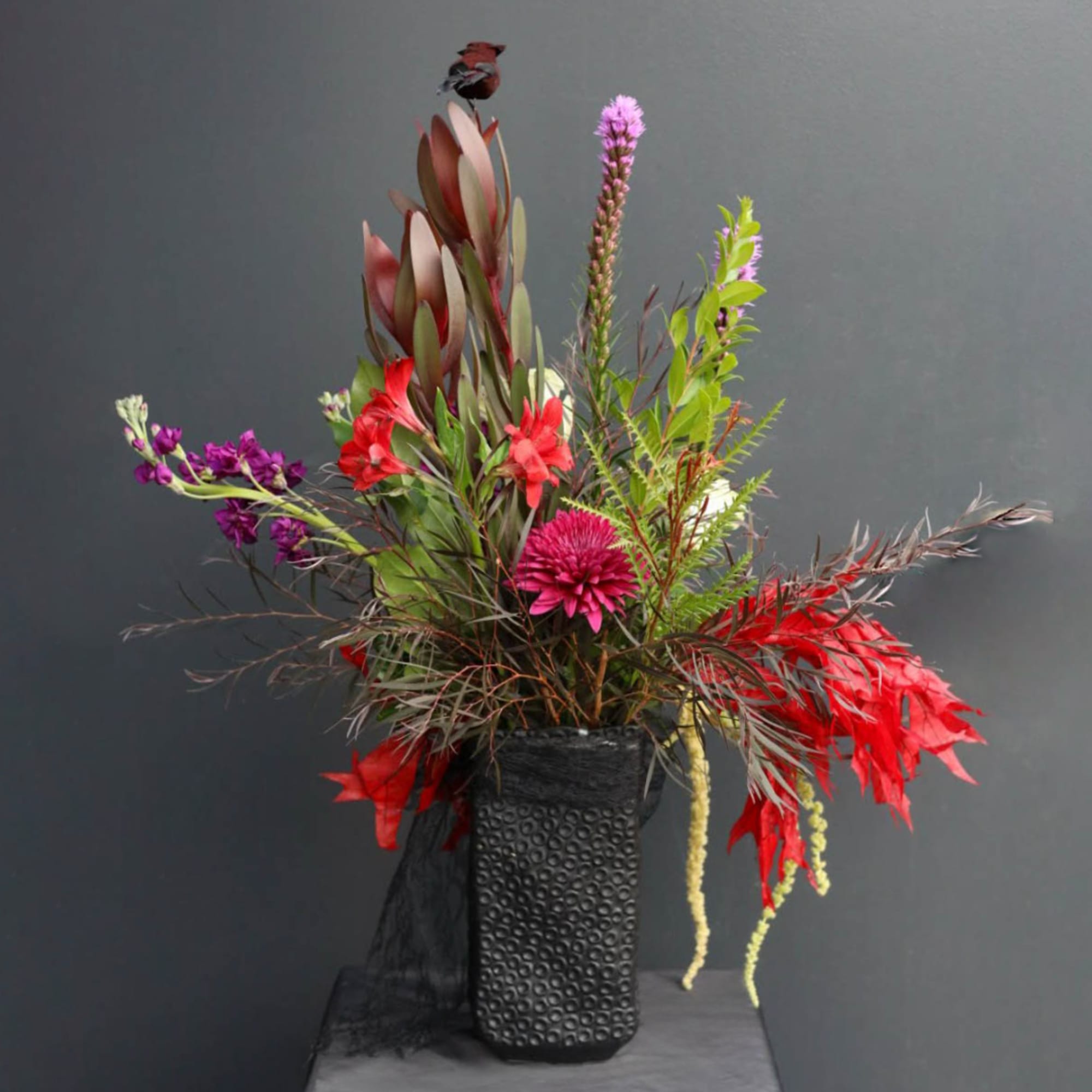 Tall mixed floral arrangement in a black textured vase with red and purple blooms