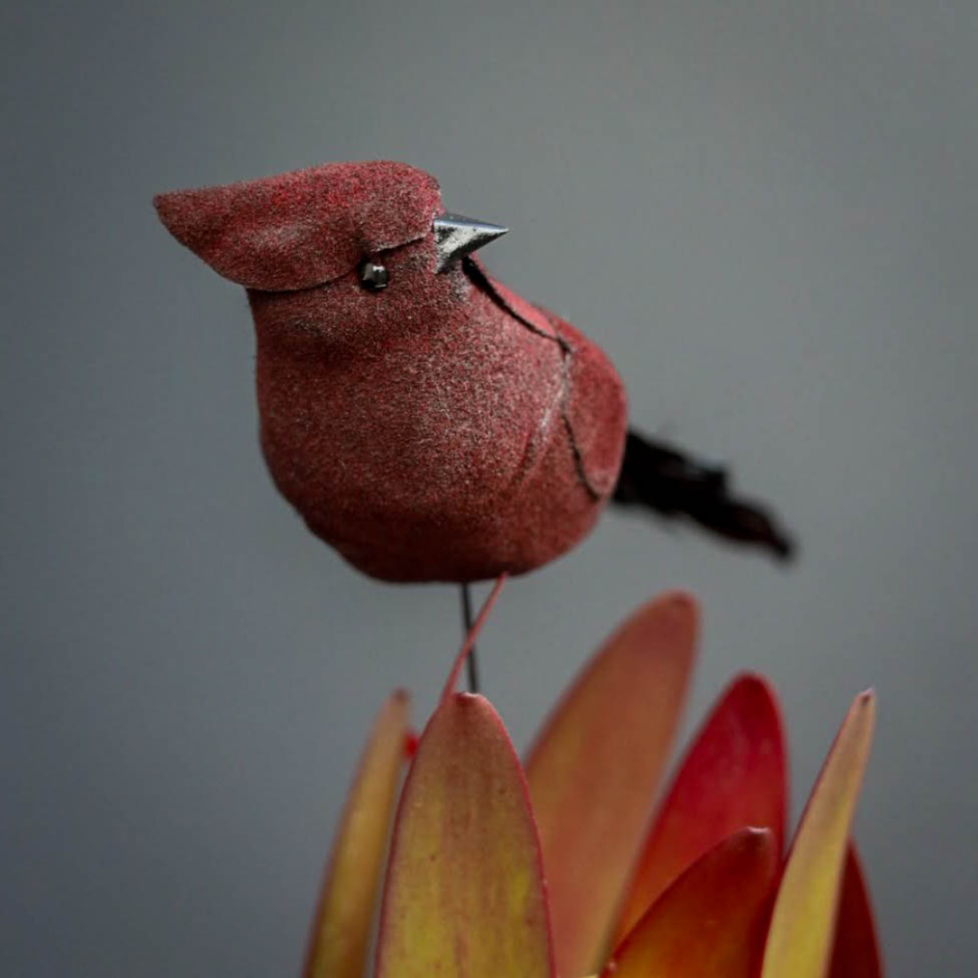 Decorative bird figurine perched above red and orange flower petals