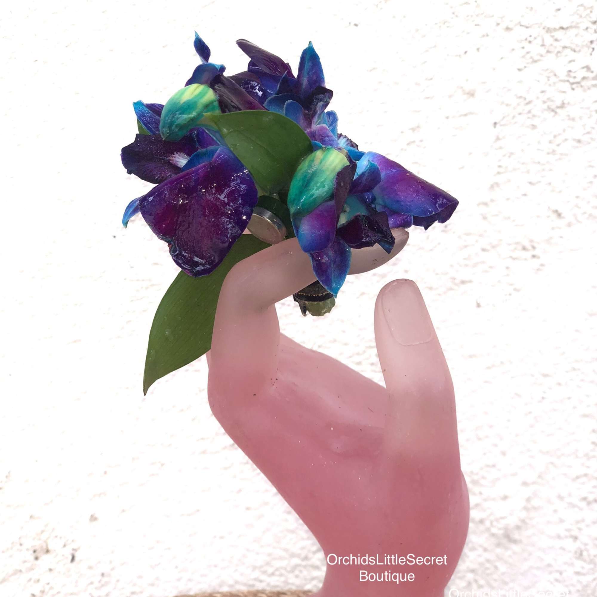 Small blue-purple orchid cluster held in a pink hand-shaped vase