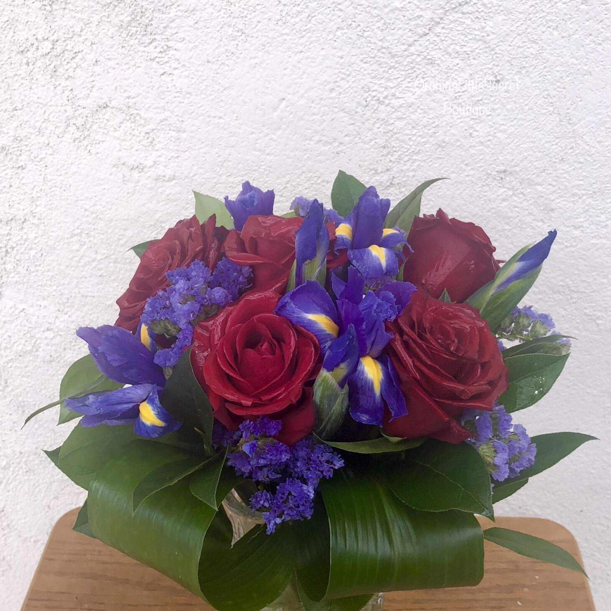 Red roses and purple irises in a clear glass vase