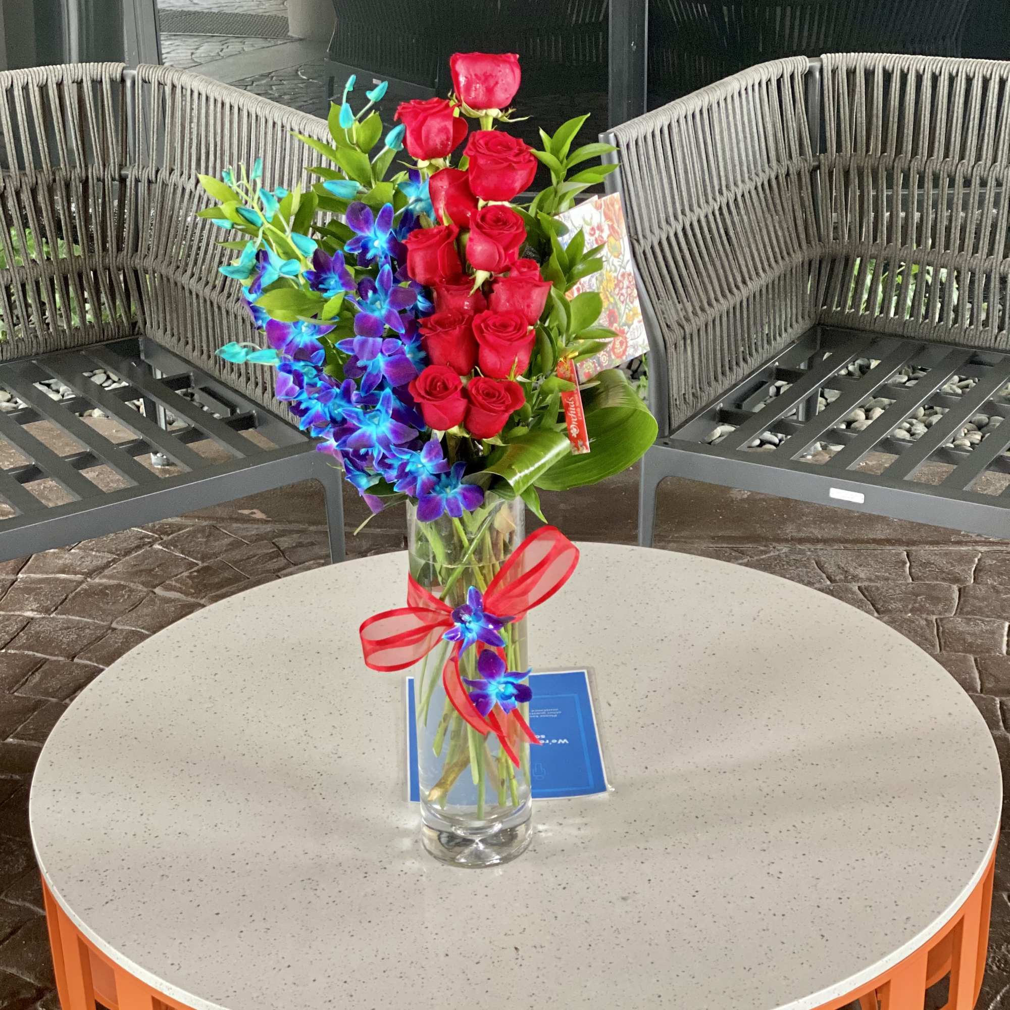 Bouquet of red roses and blue-purple orchids in a glass vase with a red ribbon