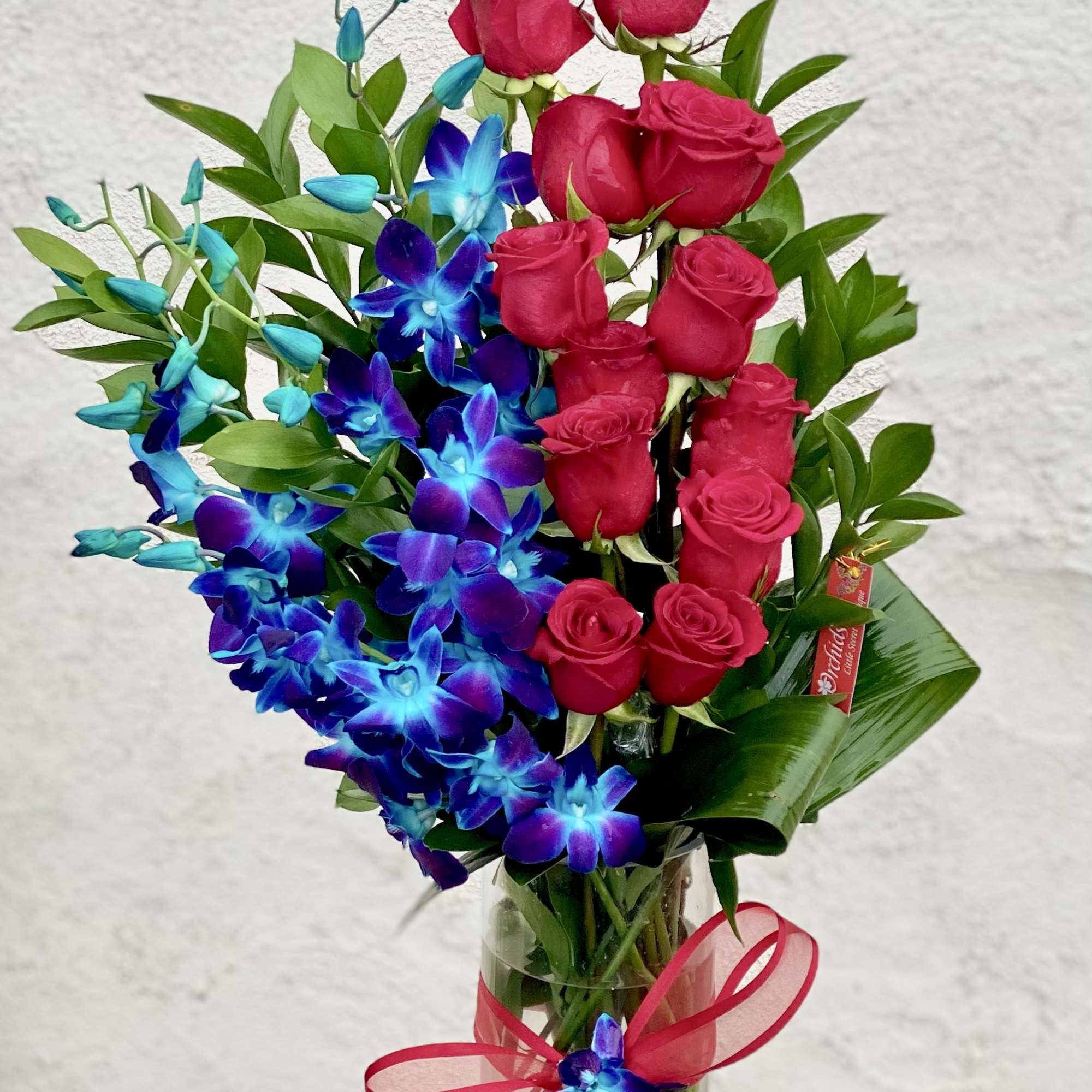 Bouquet of red roses and blue orchids in a clear glass vase with a pink ribbon