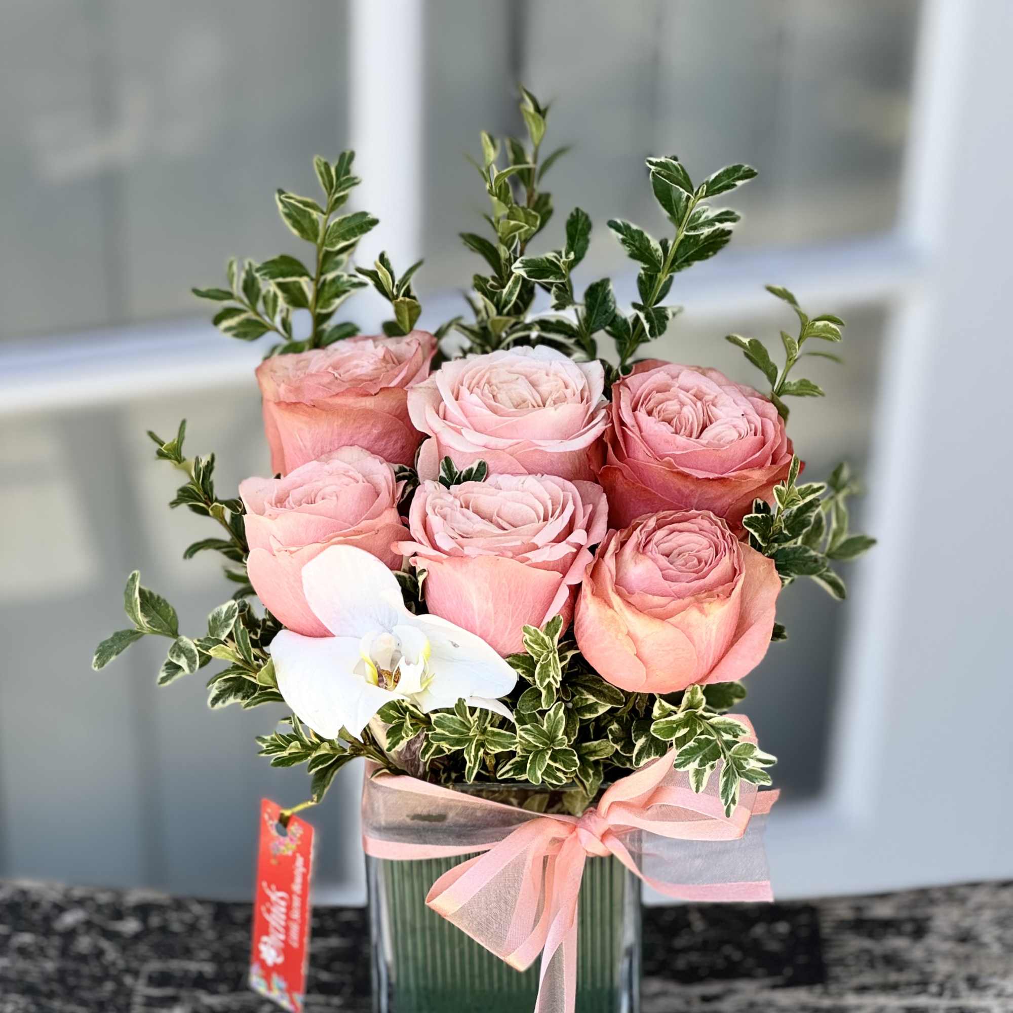 Pink roses in a glass vase with a white orchid and ribbon