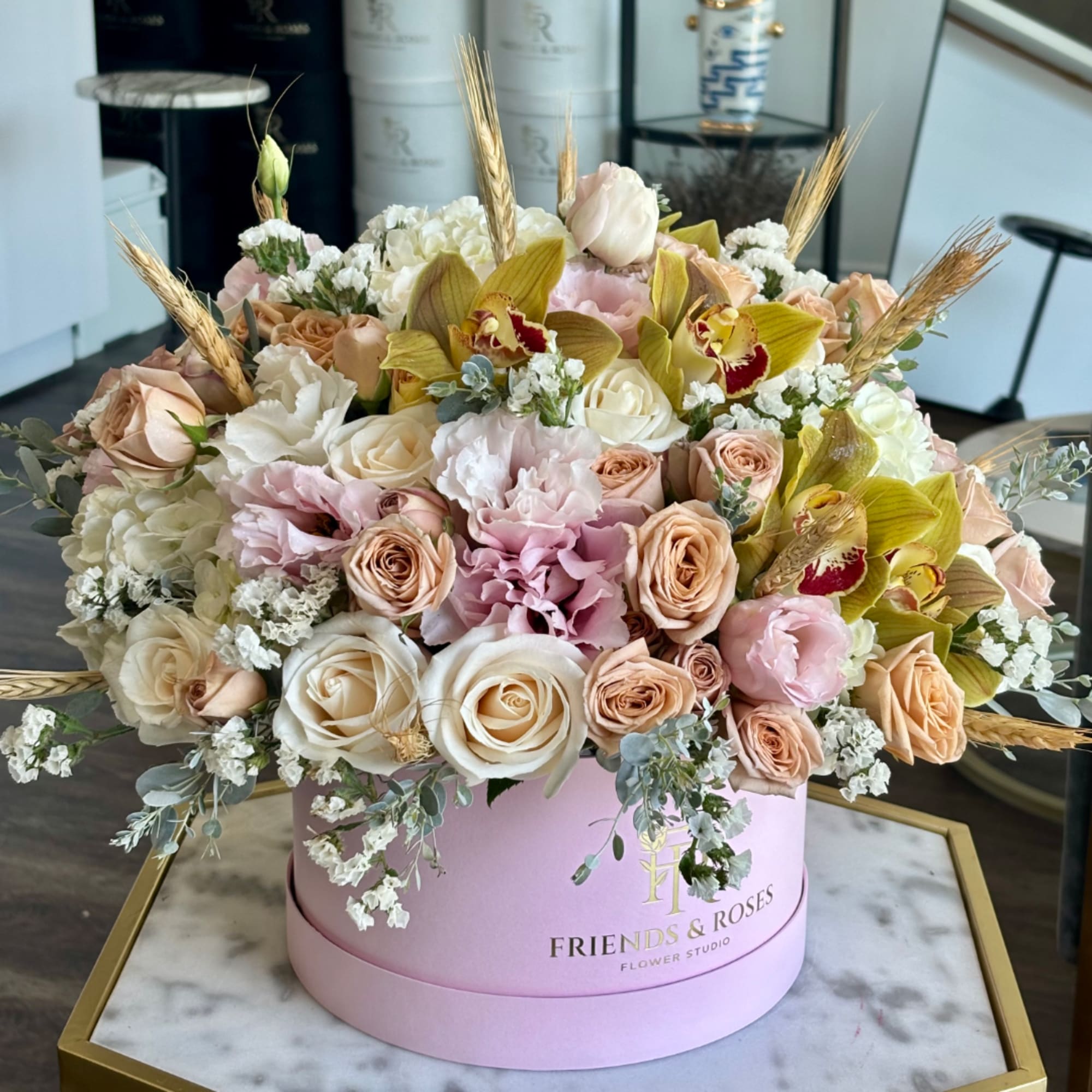 Mixed bouquet of roses, orchids, and pale pink blooms in a pink round box