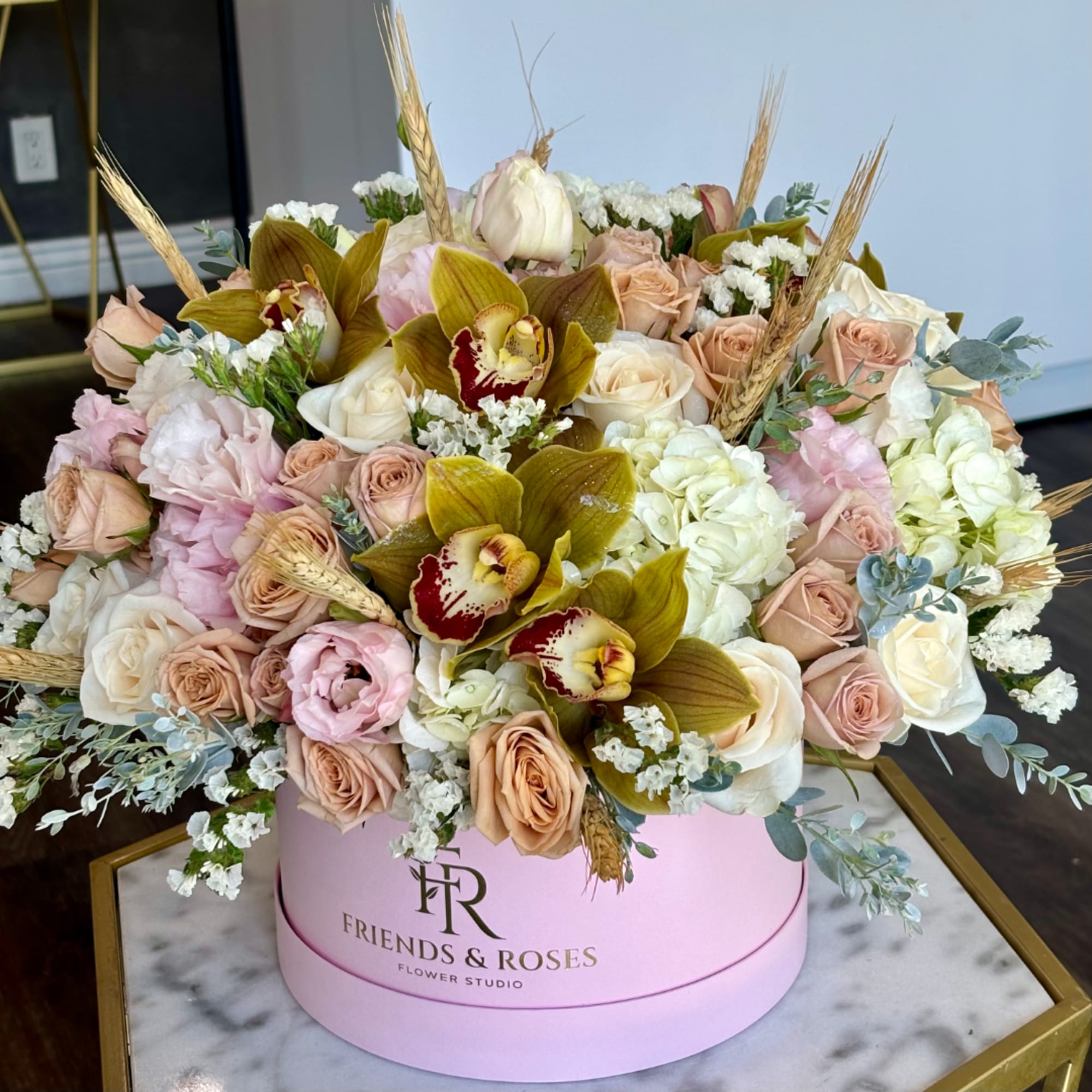 Large pastel flower arrangement in a pink round box with roses and orchids, photo 3 of 4