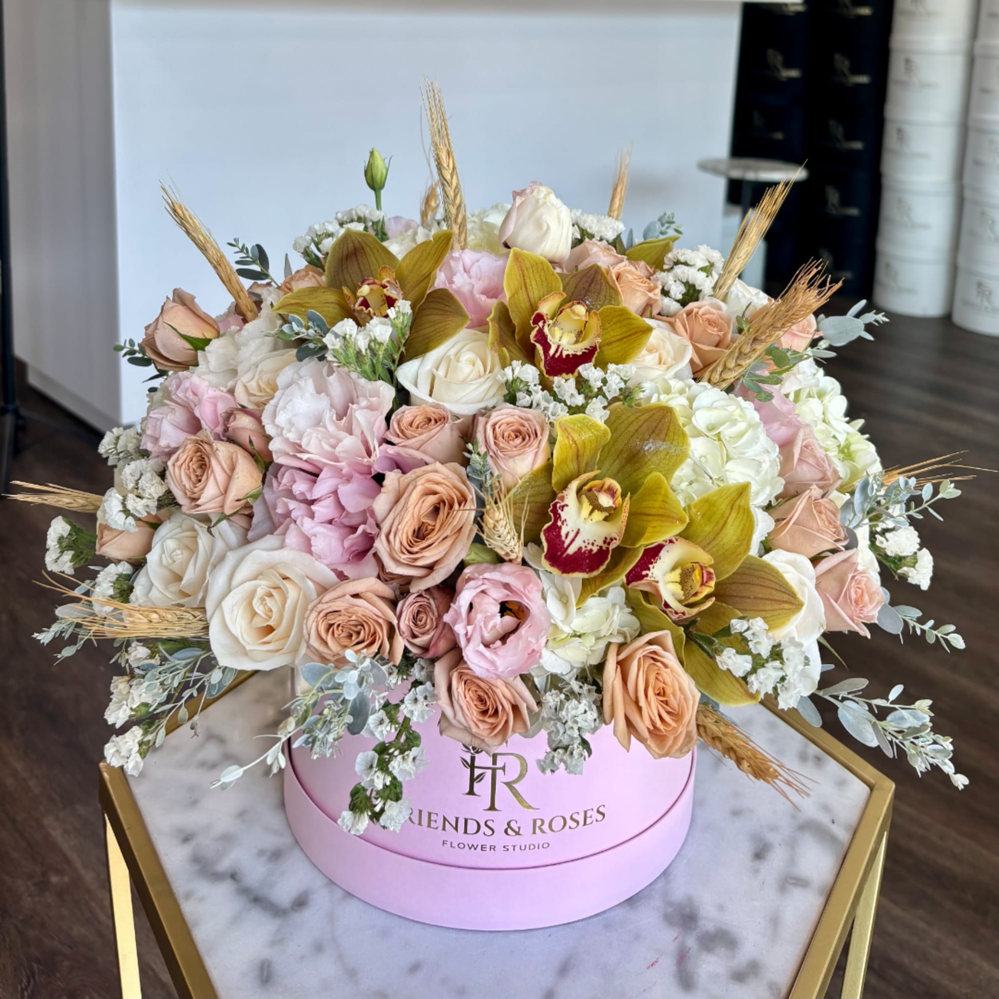 Round floral arrangement in a pink hat box with roses and orchids