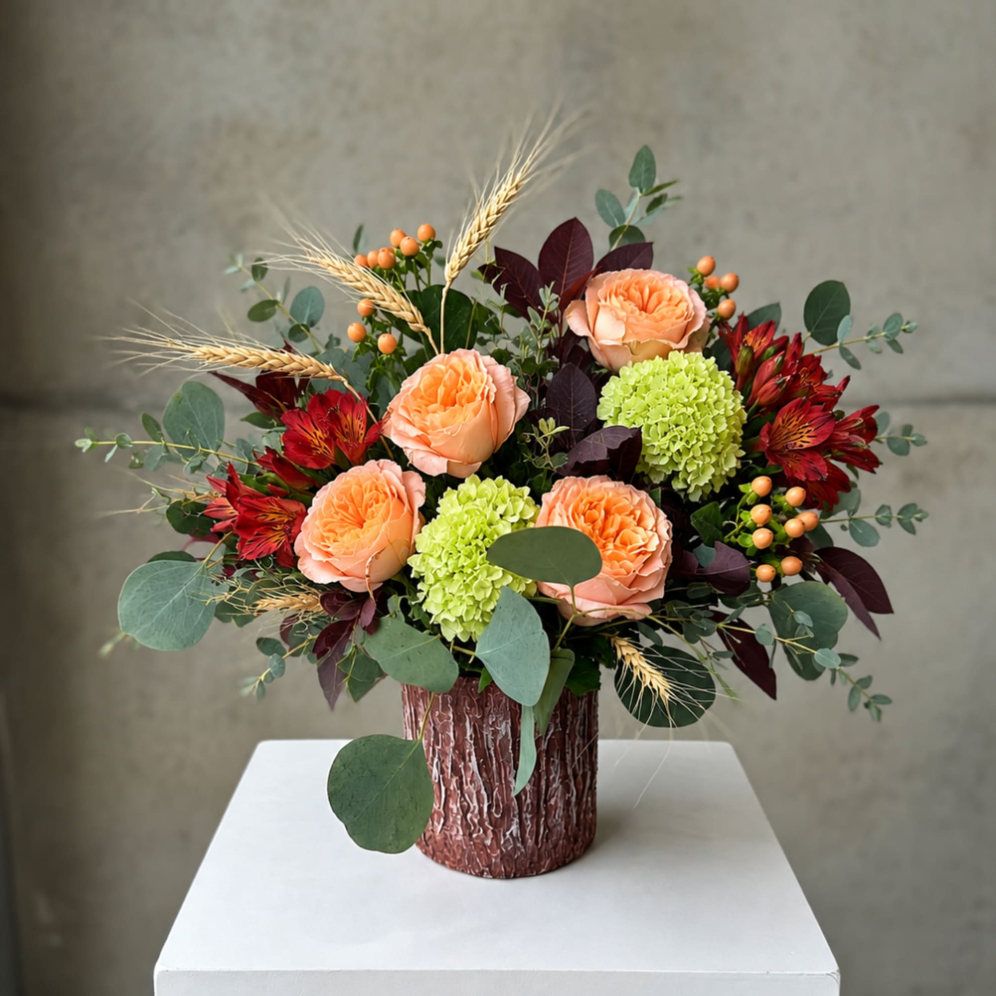 Peach roses and green hydrangeas in a textured vase with red blooms