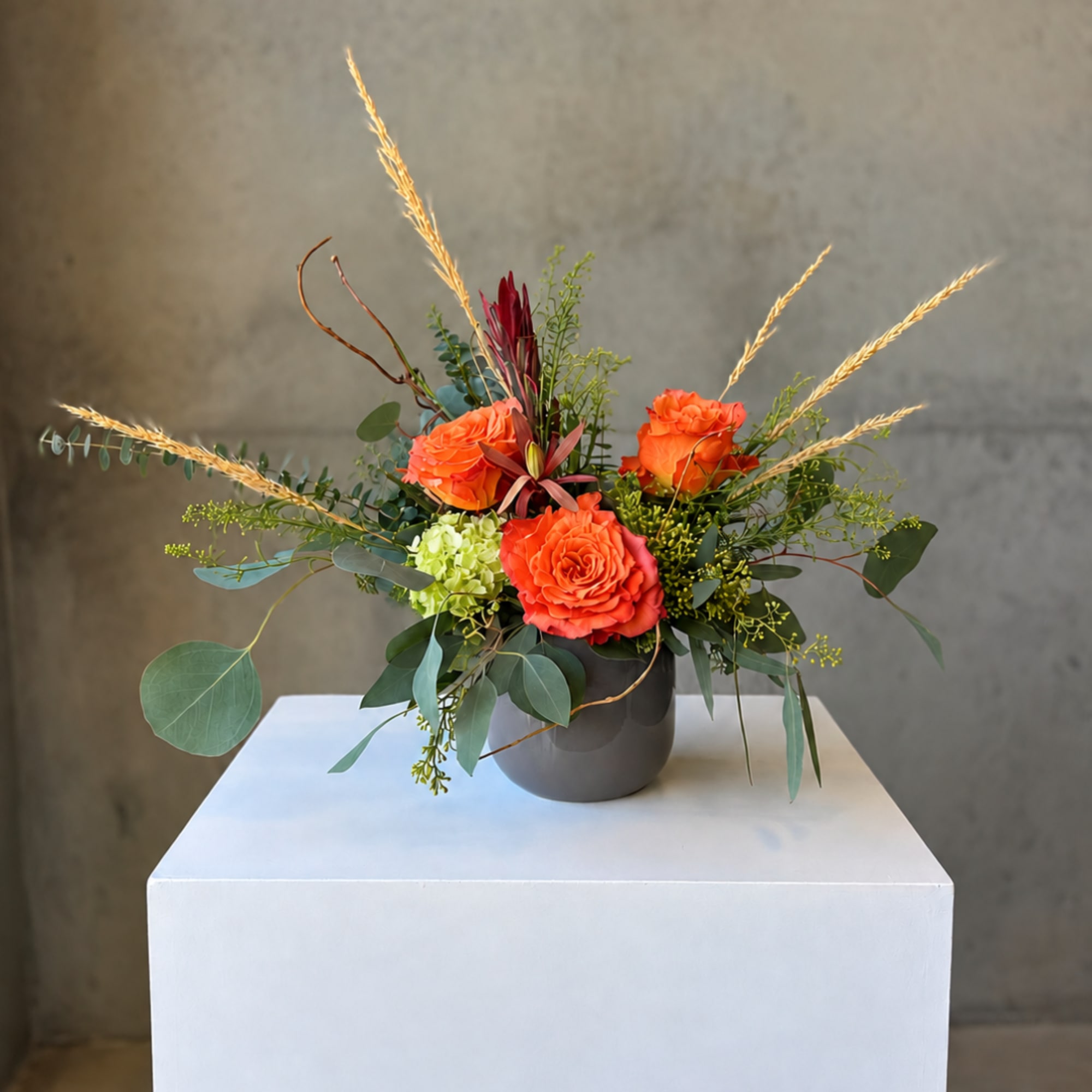 Orange roses in a dark vase with airy greenery and tall wheat stems