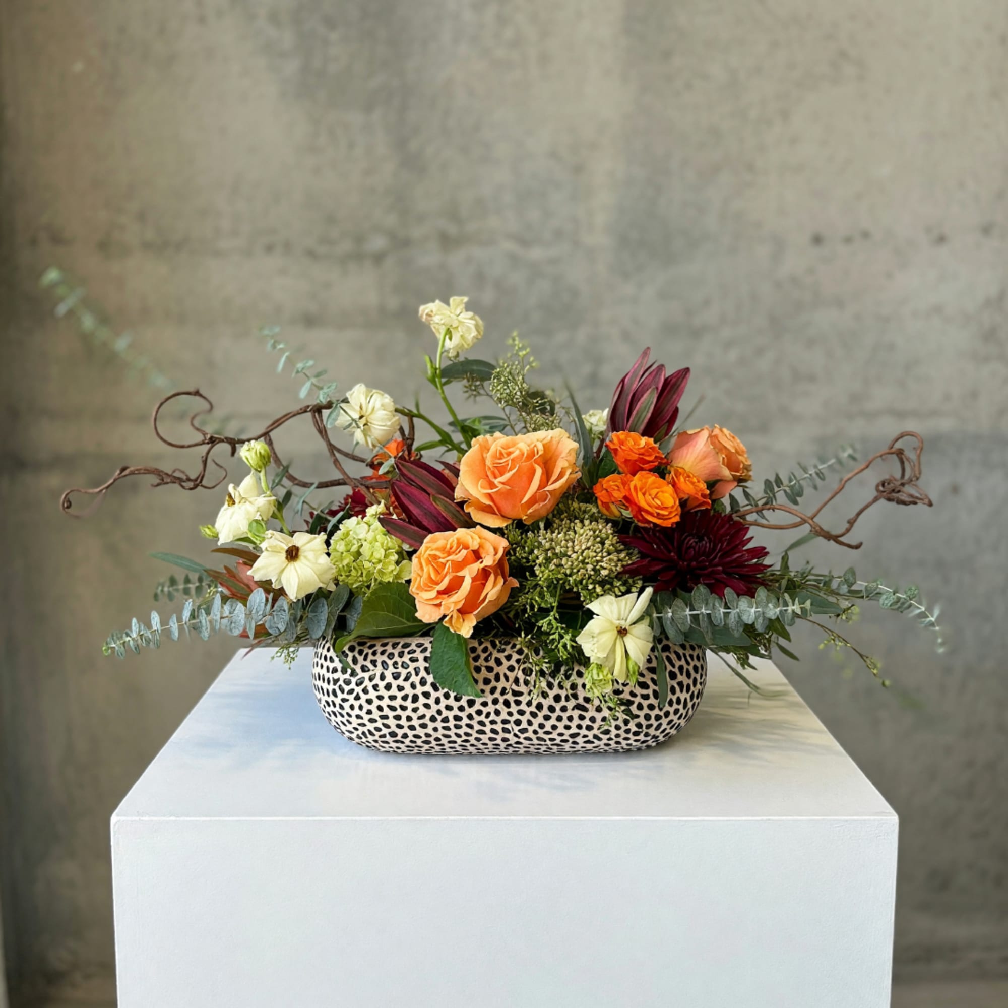 Orange roses and burgundy flowers in a patterned low vase