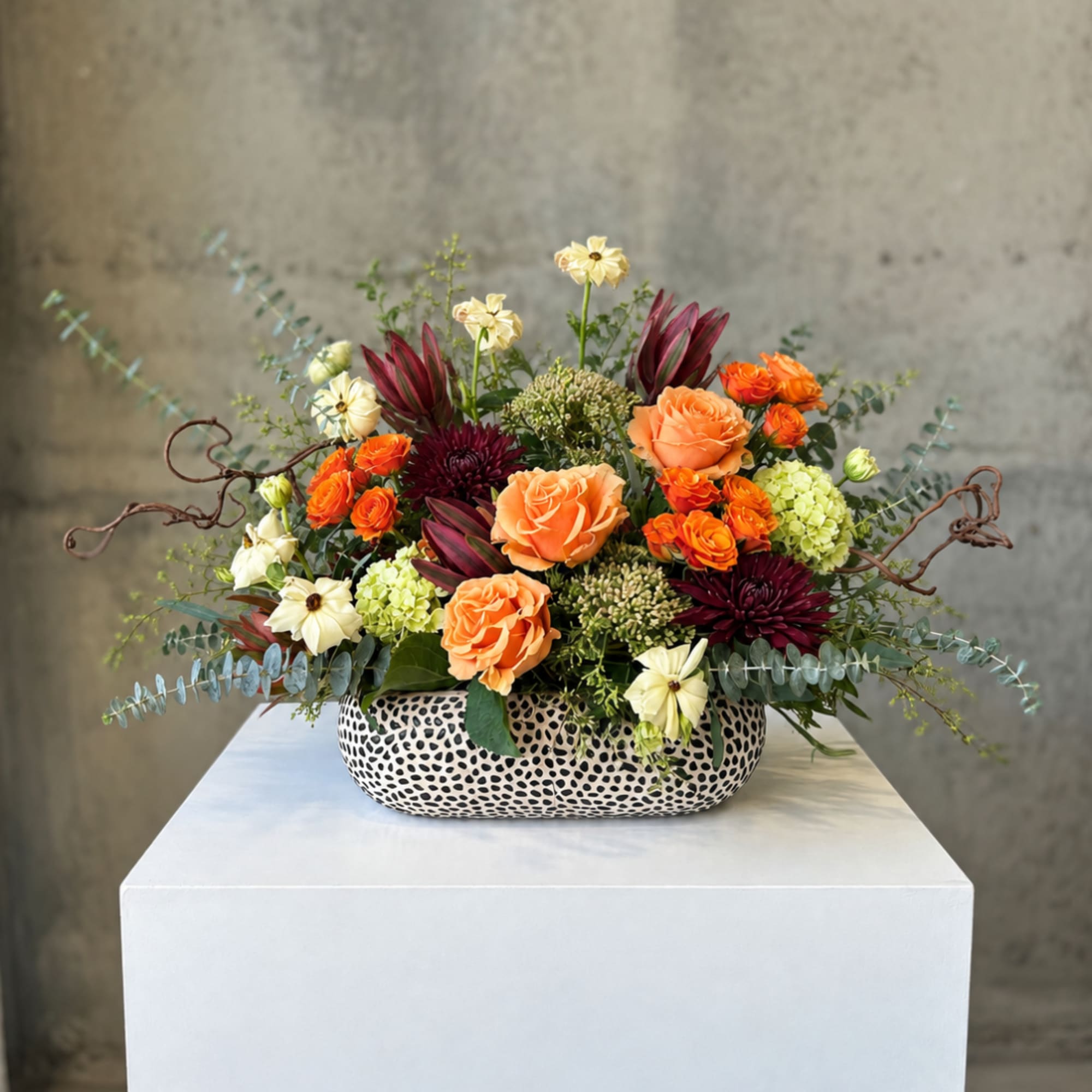 Mixed floral arrangement in a patterned ceramic vase with orange and cream blooms