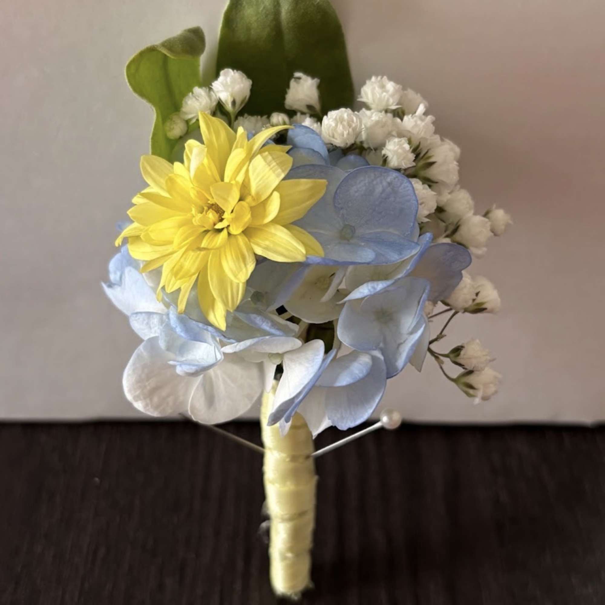 Small boutonniere with yellow and blue flowers and white accents