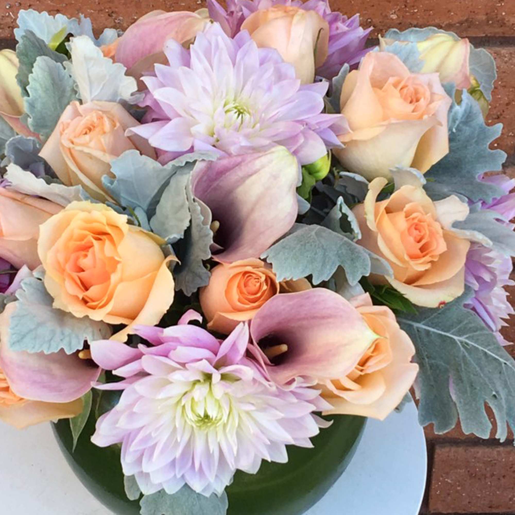Peach roses, lavender mums, and pink calla lilies in a green vase