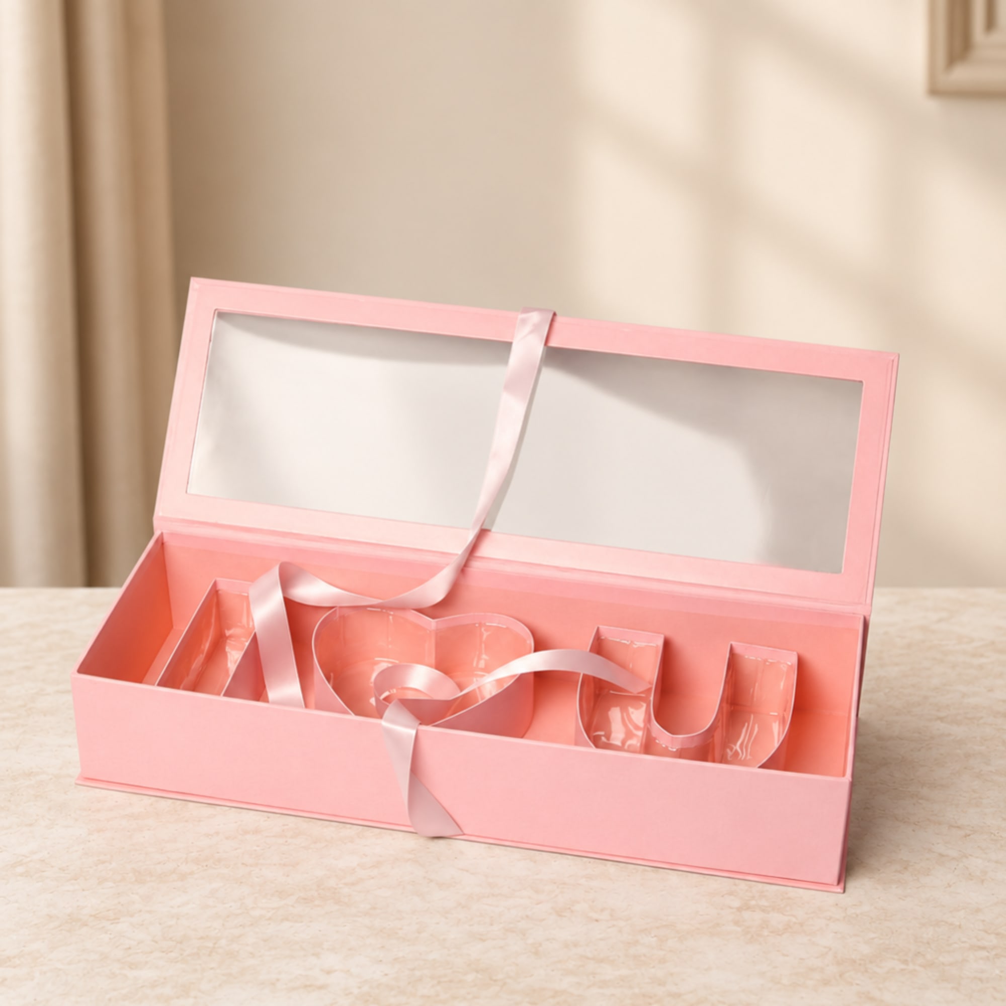 Pink gift box with a clear lid and ribbon, holding the word LOVE