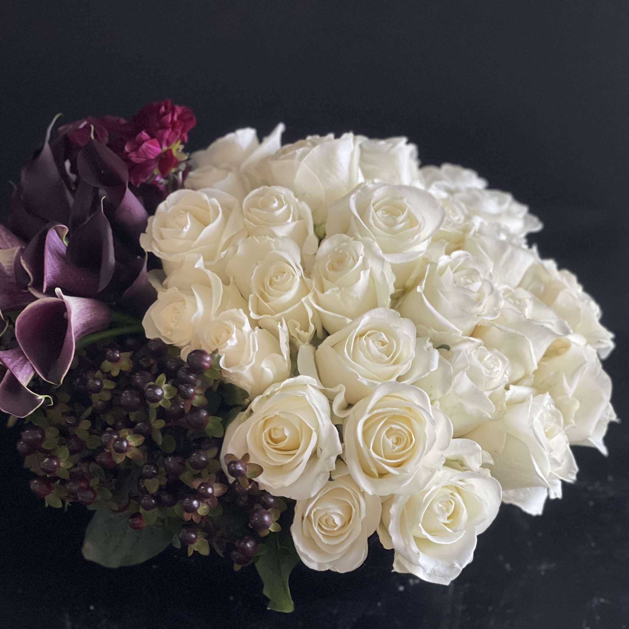 Low arrangement of white roses with dark purple calla lilies and berries