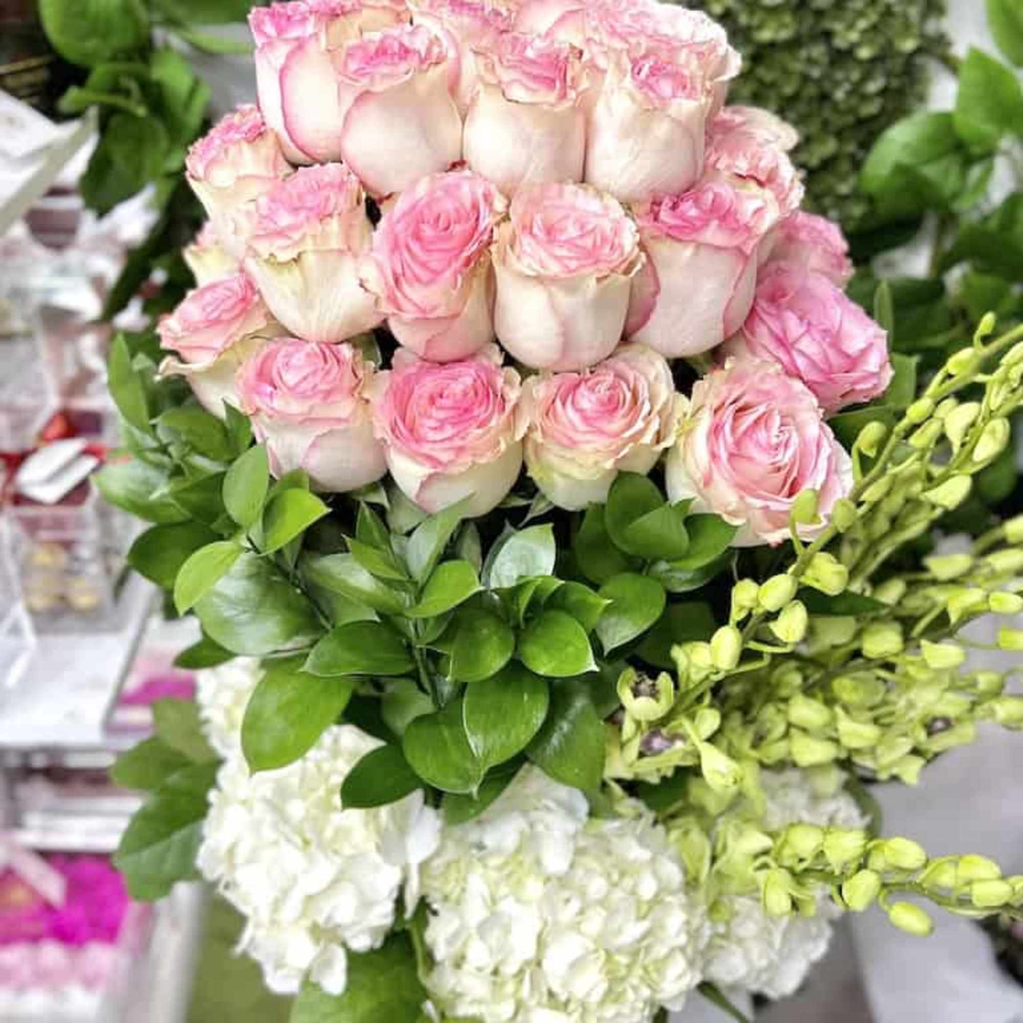 Tall arrangement of pink-tipped white roses with white hydrangeas and green orchid stems