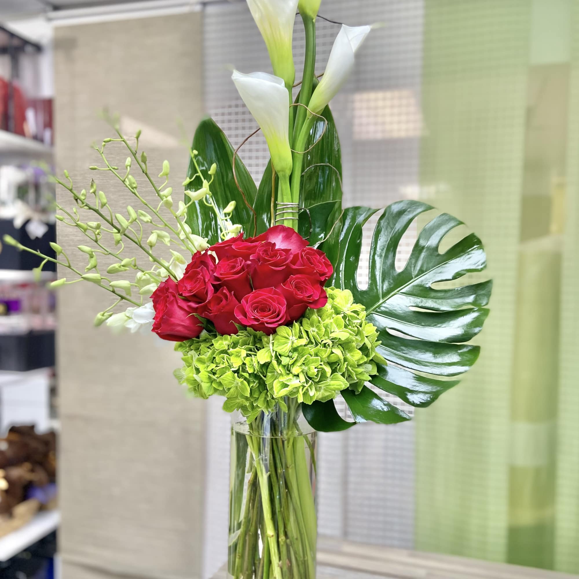 Tall arrangement of white calla lilies, red roses, and green hydrangeas in a clear glass cylinder vase