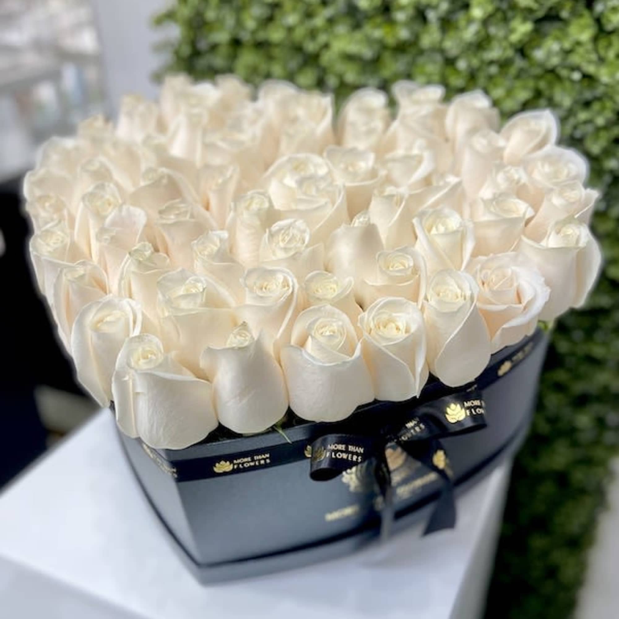 Heart-shaped black box filled with tightly packed ivory roses on a white pedestal