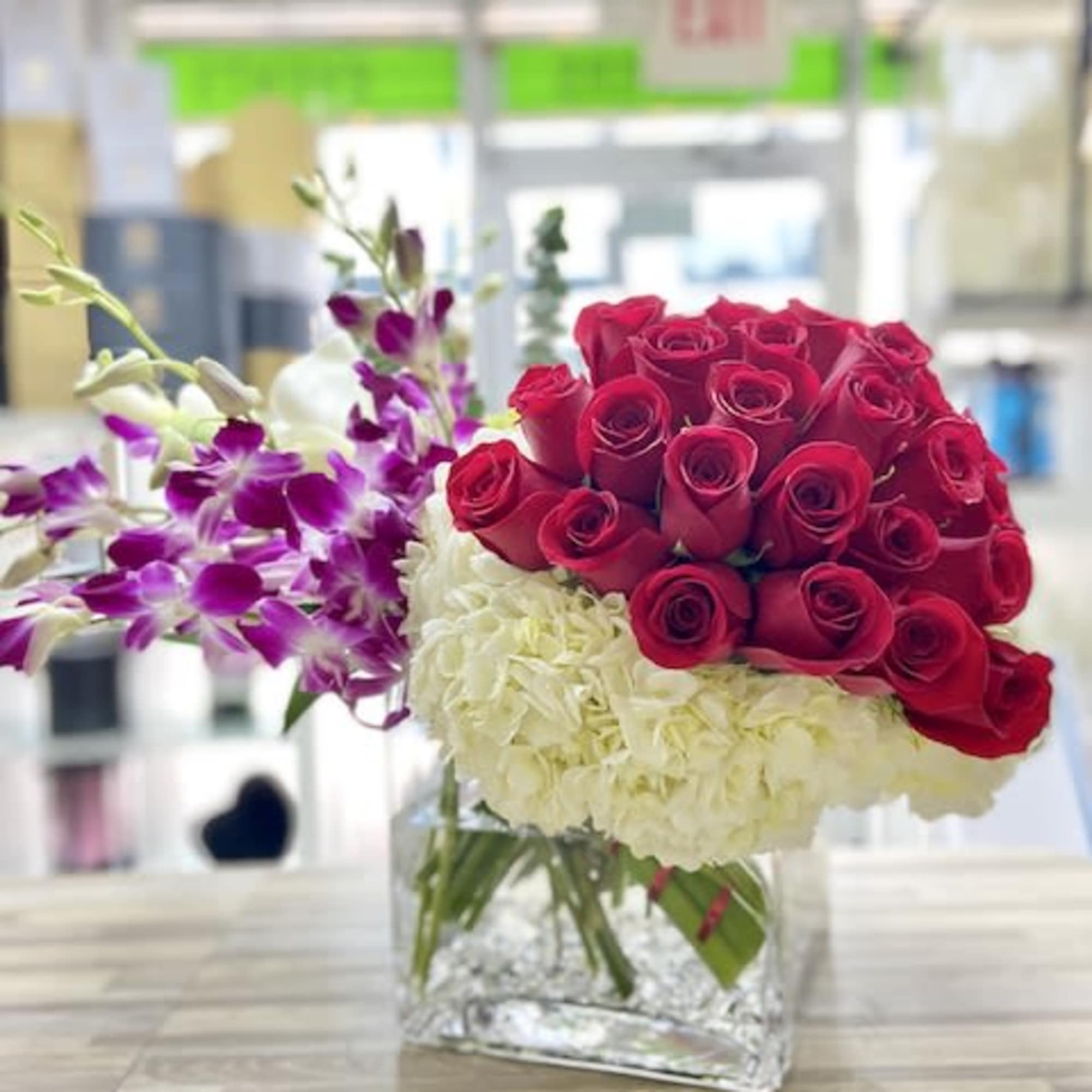 Low arrangement of red roses, white hydrangeas, and purple orchids in a clear glass cube vase