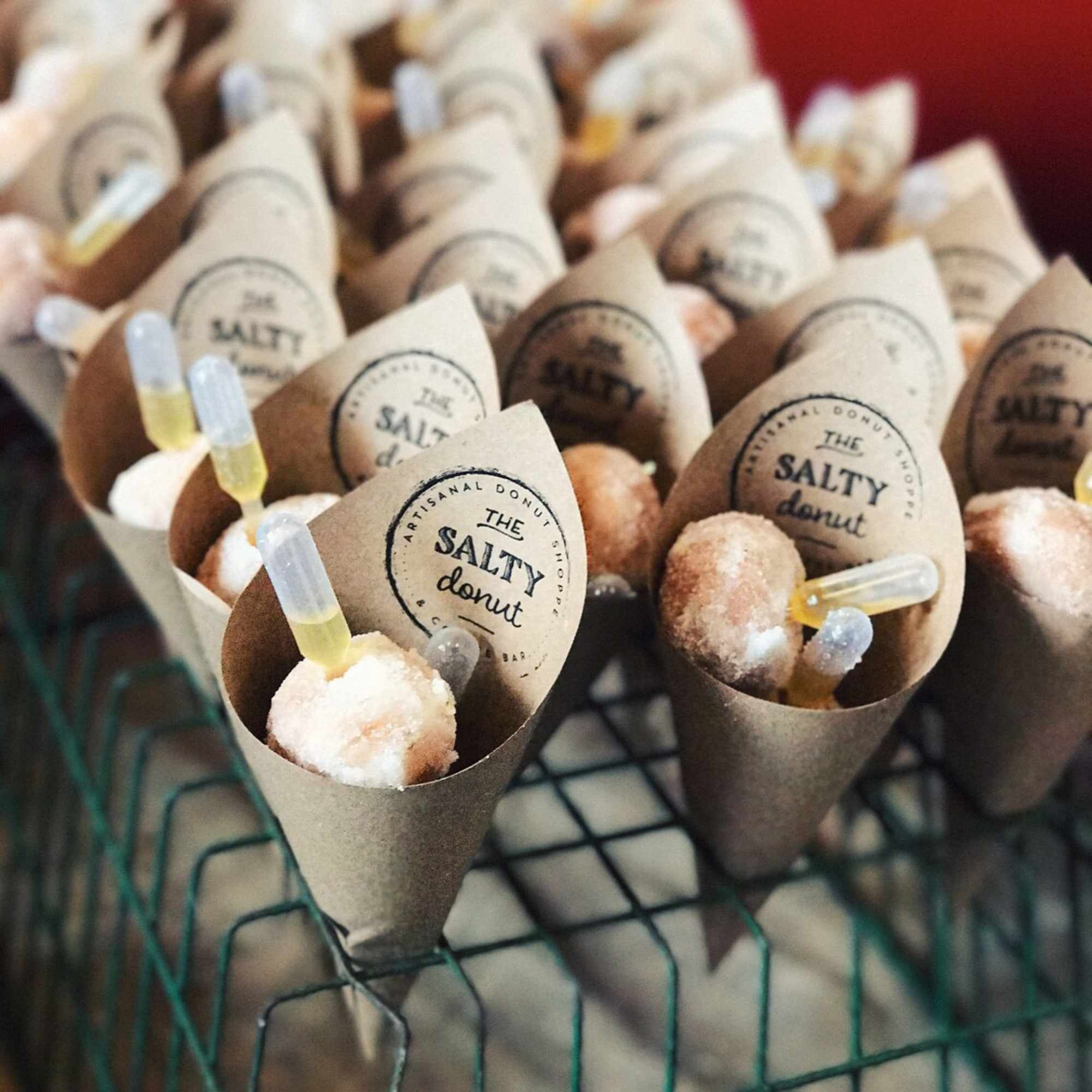 Mini donuts in kraft paper cones with small droppers on a rack