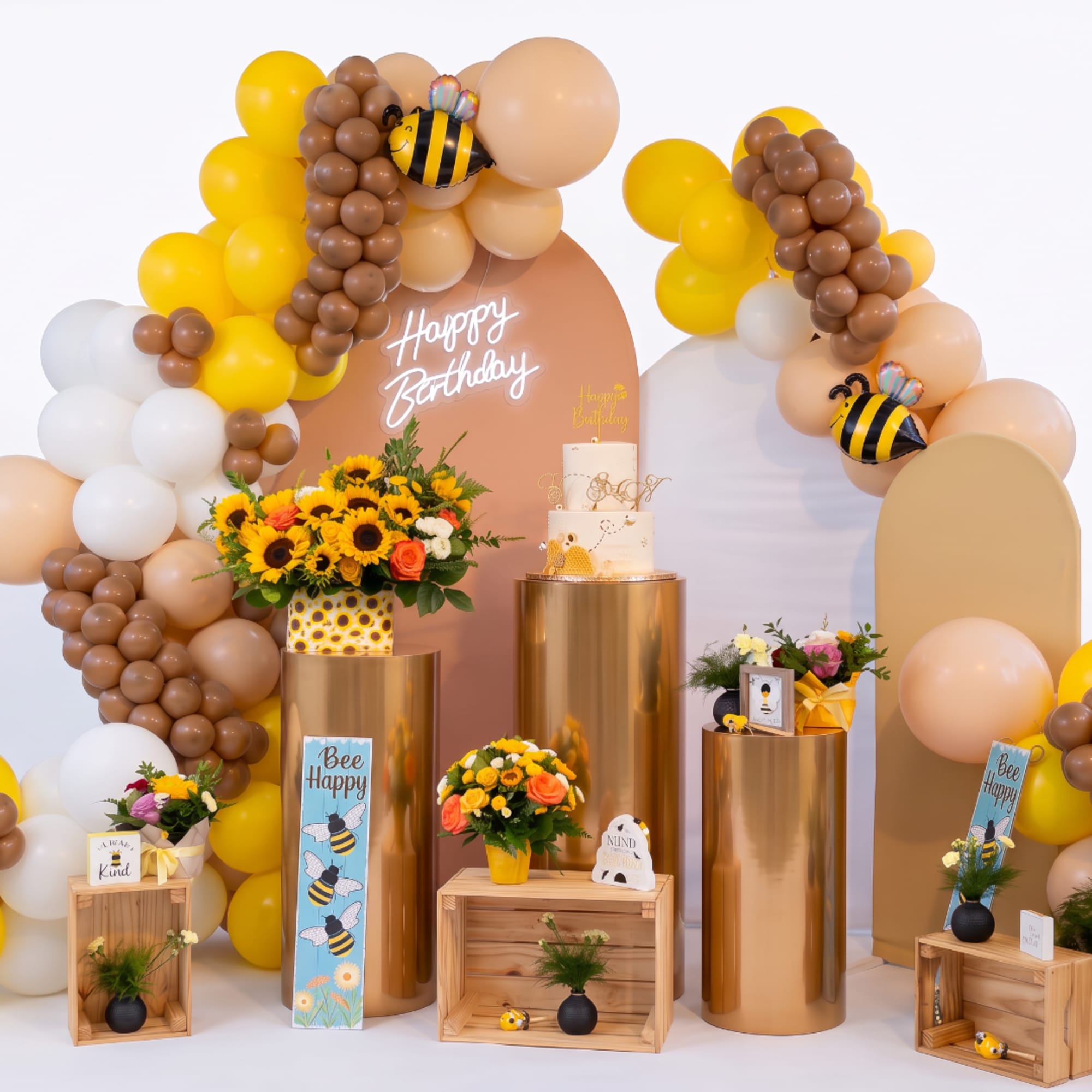 Birthday display with balloon arches, sunflowers, and a cake on gold pedestals
