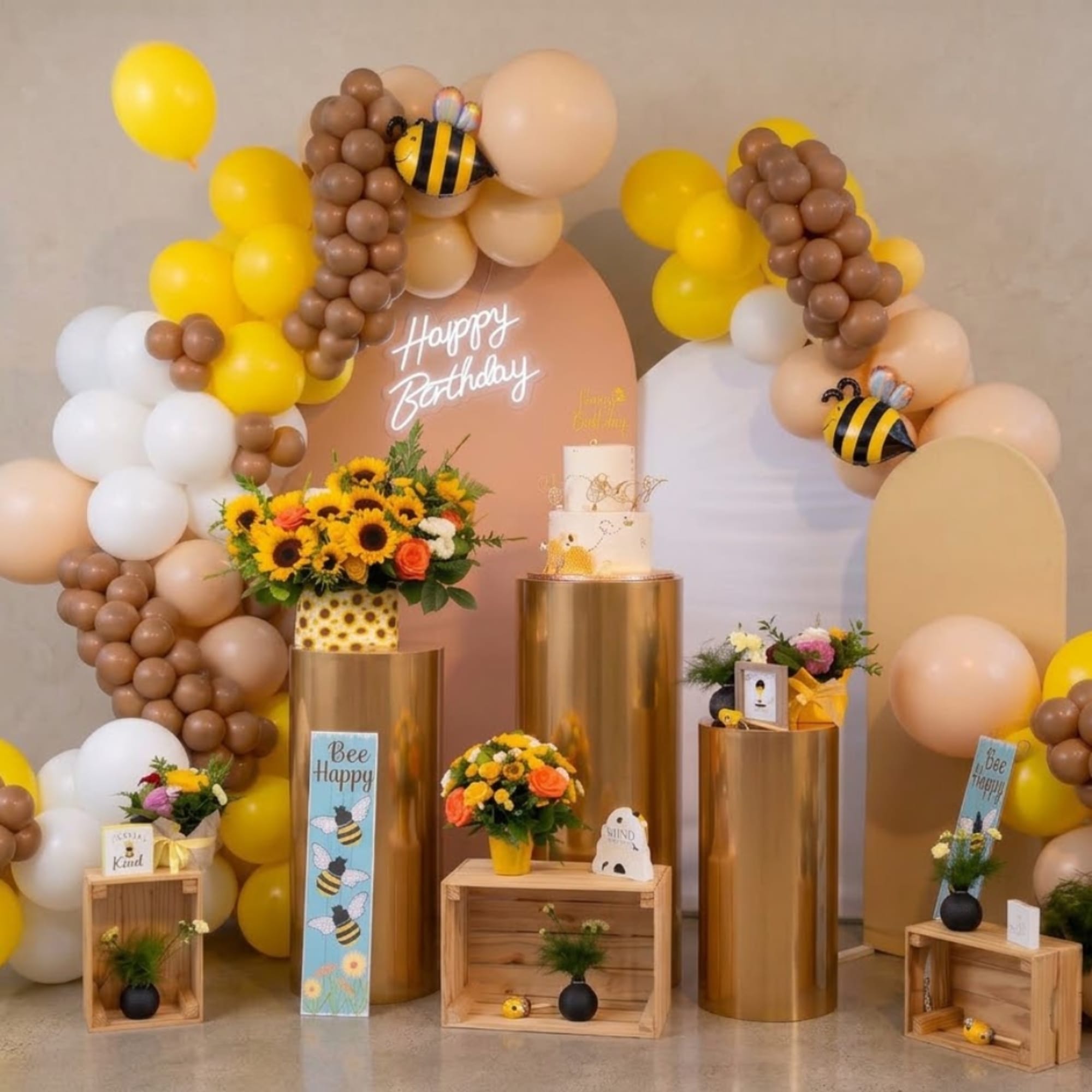 Birthday display with balloon arches, sunflower arrangements, and cake stands