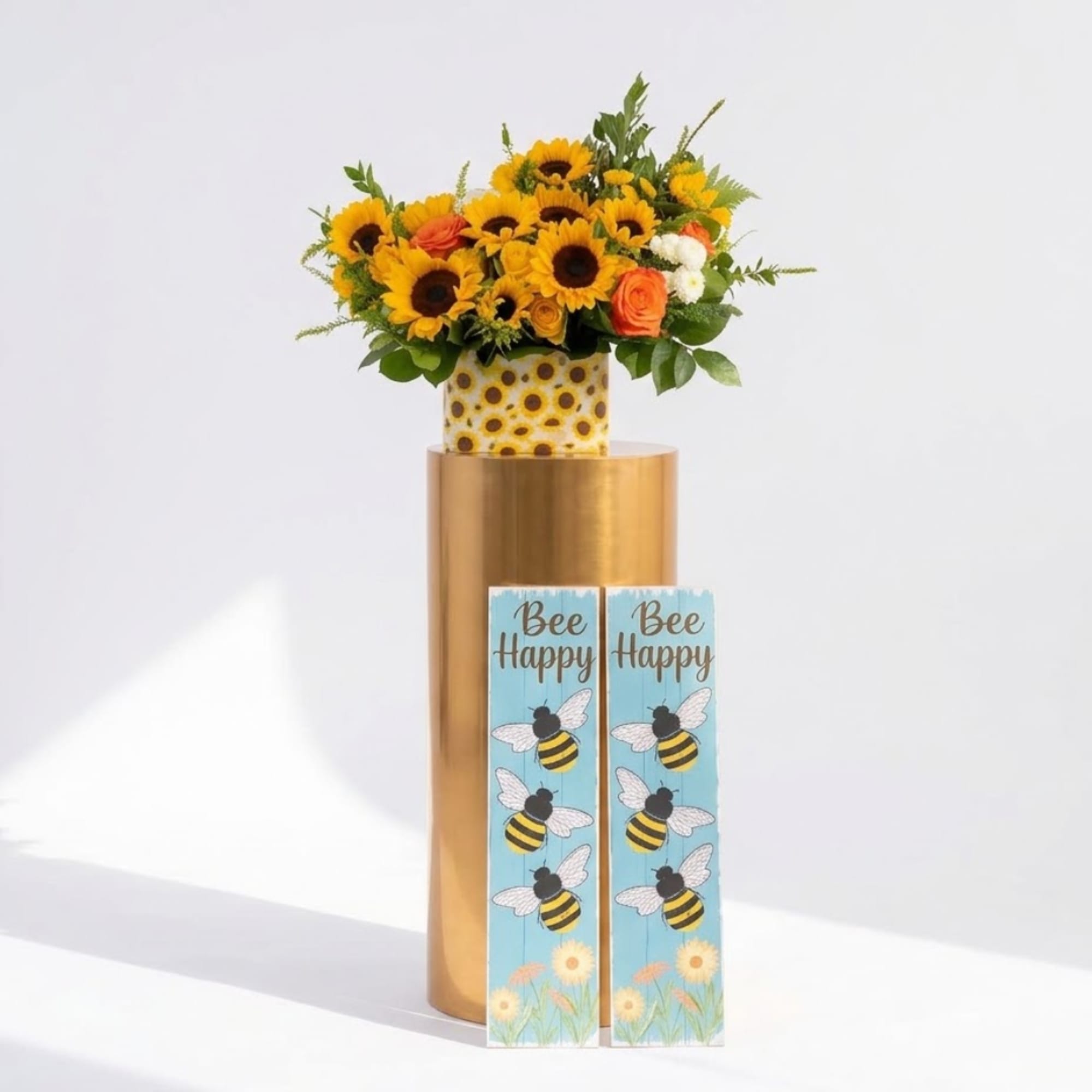 Sunflower and orange rose arrangement in a gold vase with bee-themed signs