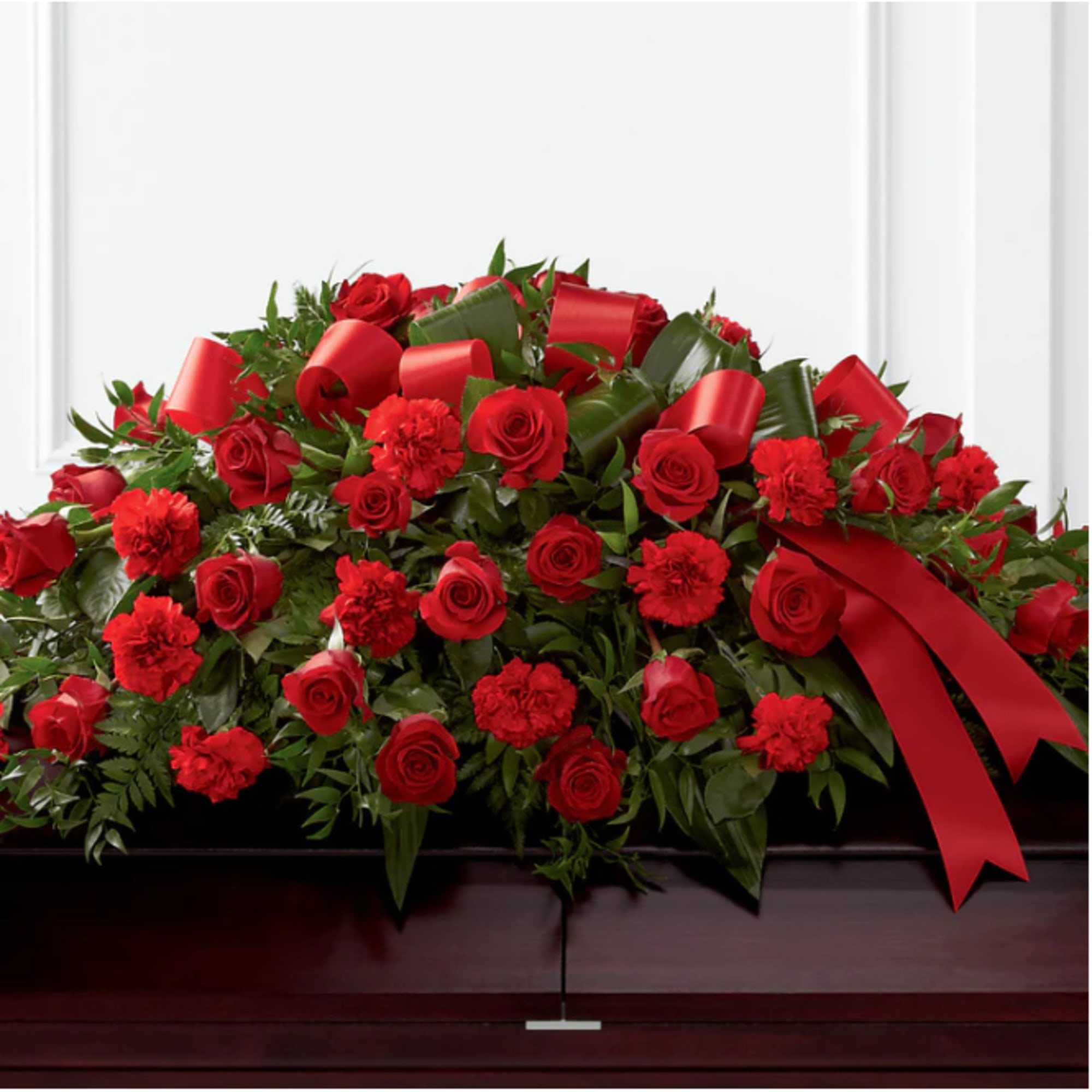 Red roses and carnations arranged on a casket with red ribbon