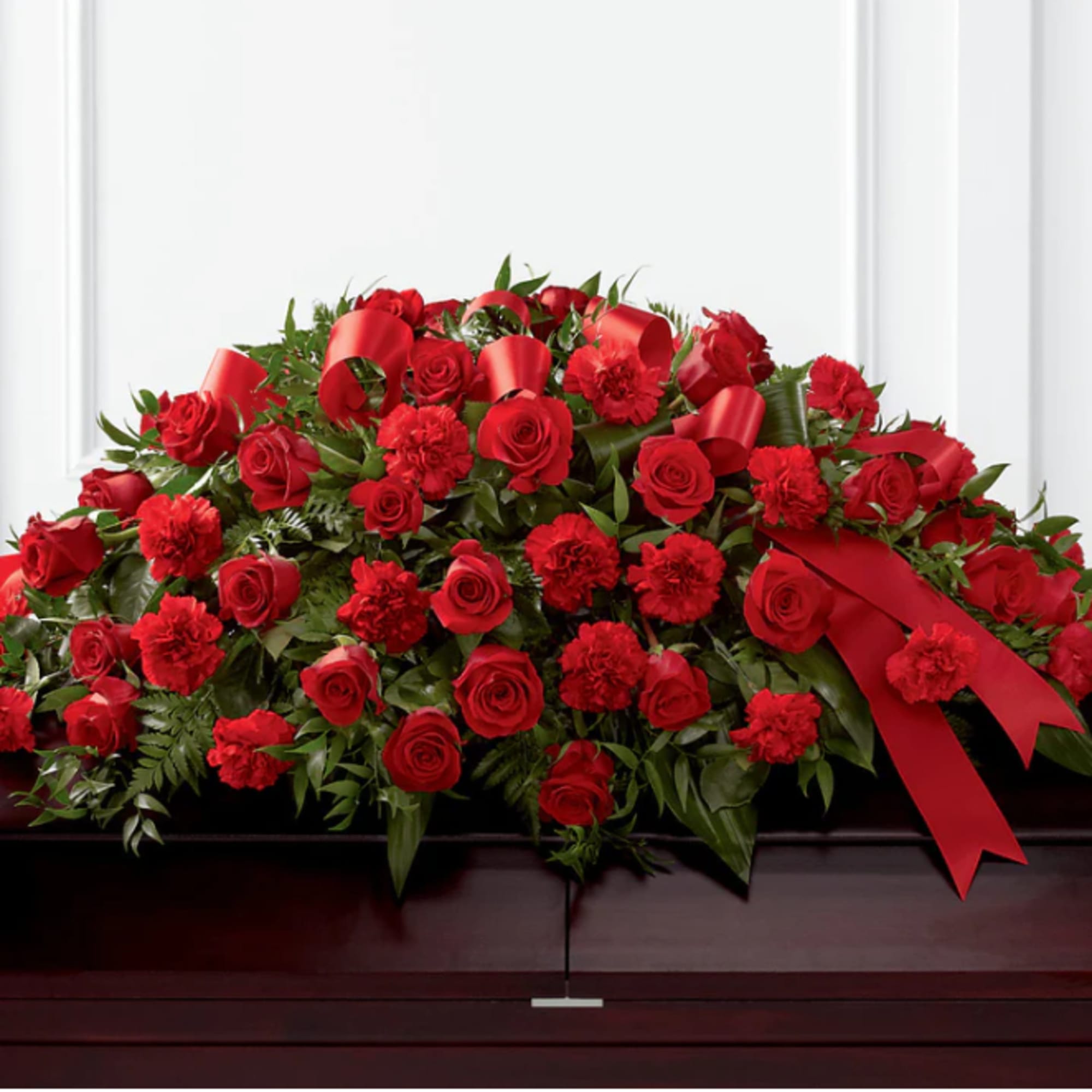 Red roses and carnations arranged on a casket with red ribbon