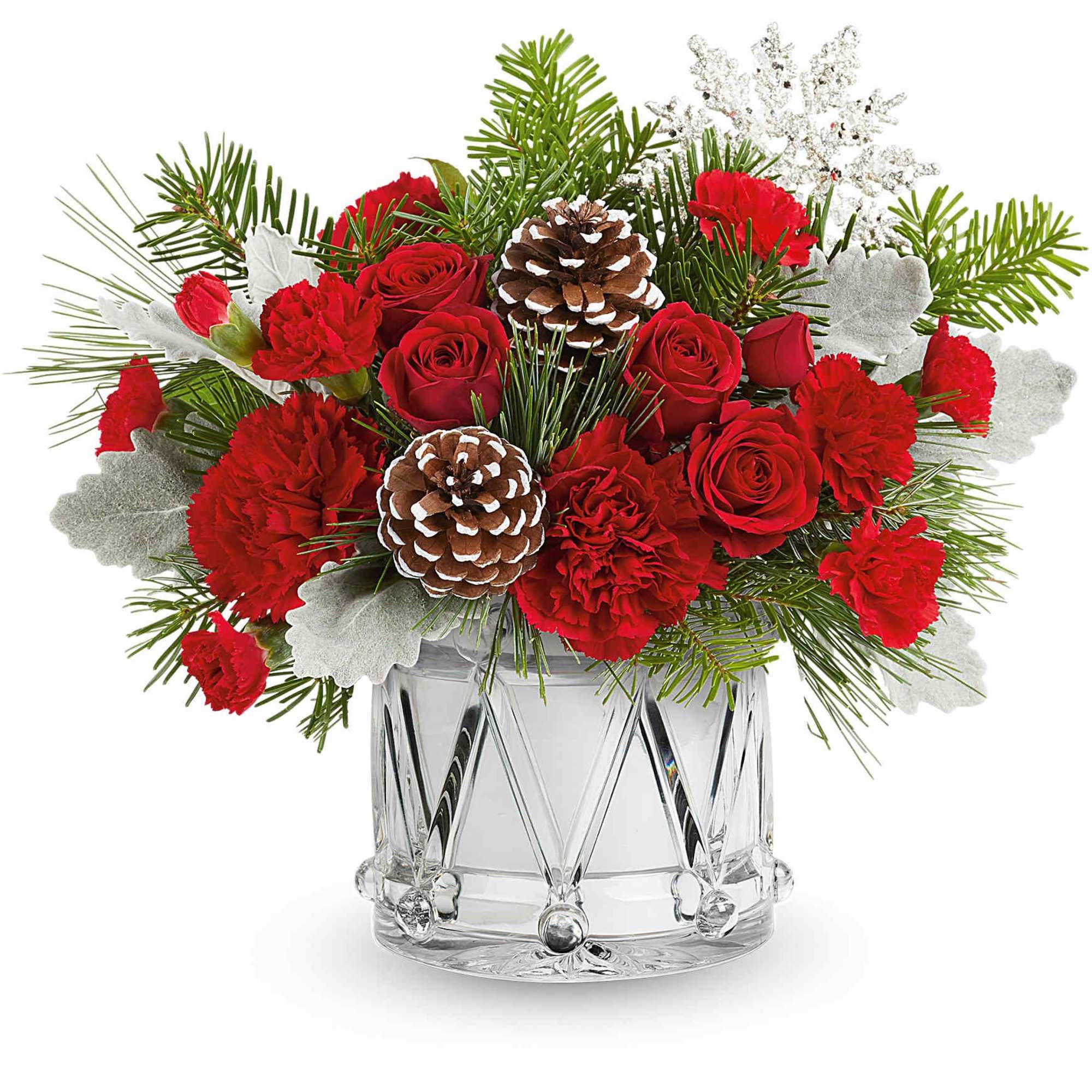 Red roses and carnations in a clear glass vase with pinecones and winter greenery