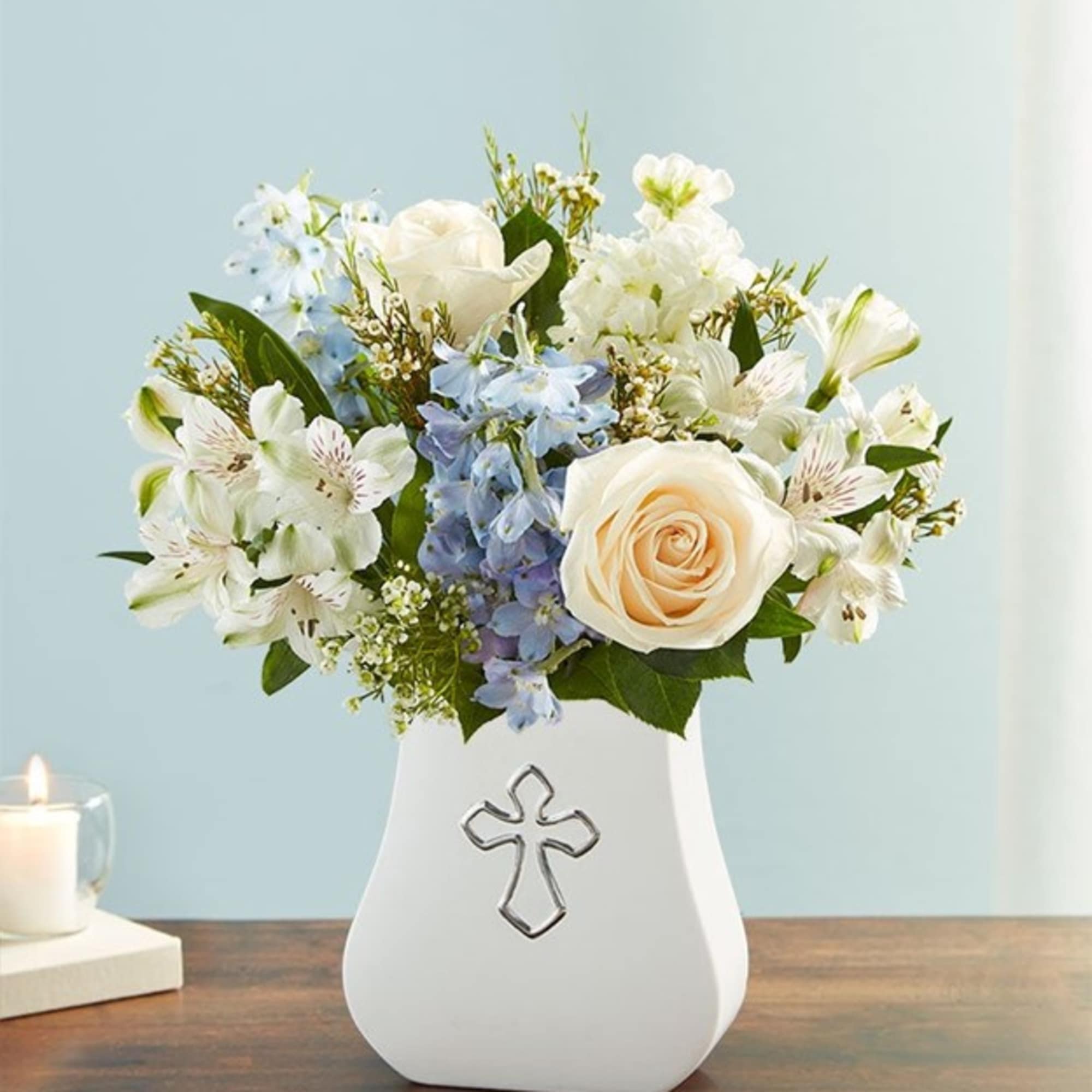White and blue floral arrangement in a white vase with a cross emblem
