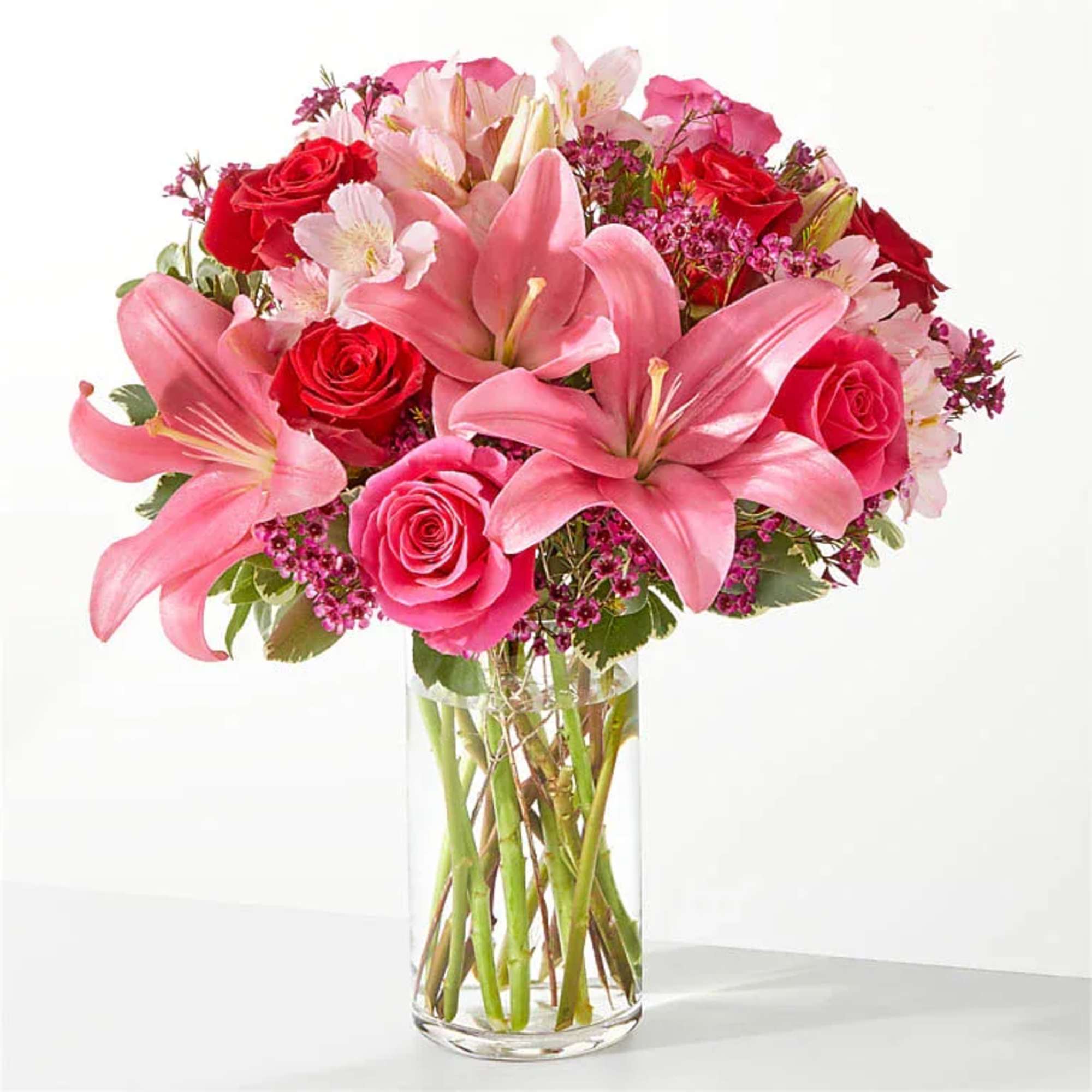 Pink lilies and red roses arranged in a clear glass vase