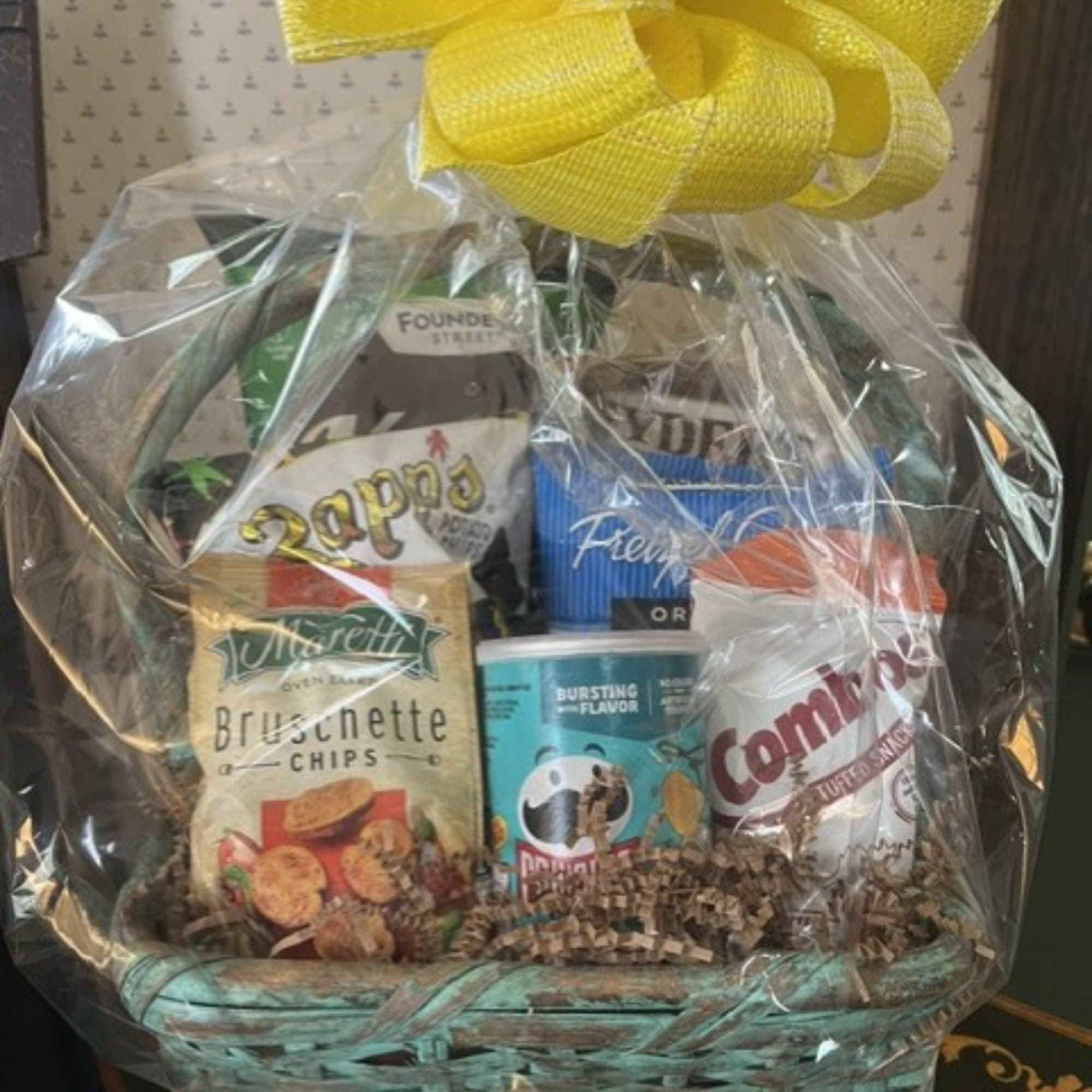 Gift basket with assorted snack packages wrapped in clear plastic and topped with a yellow bow
