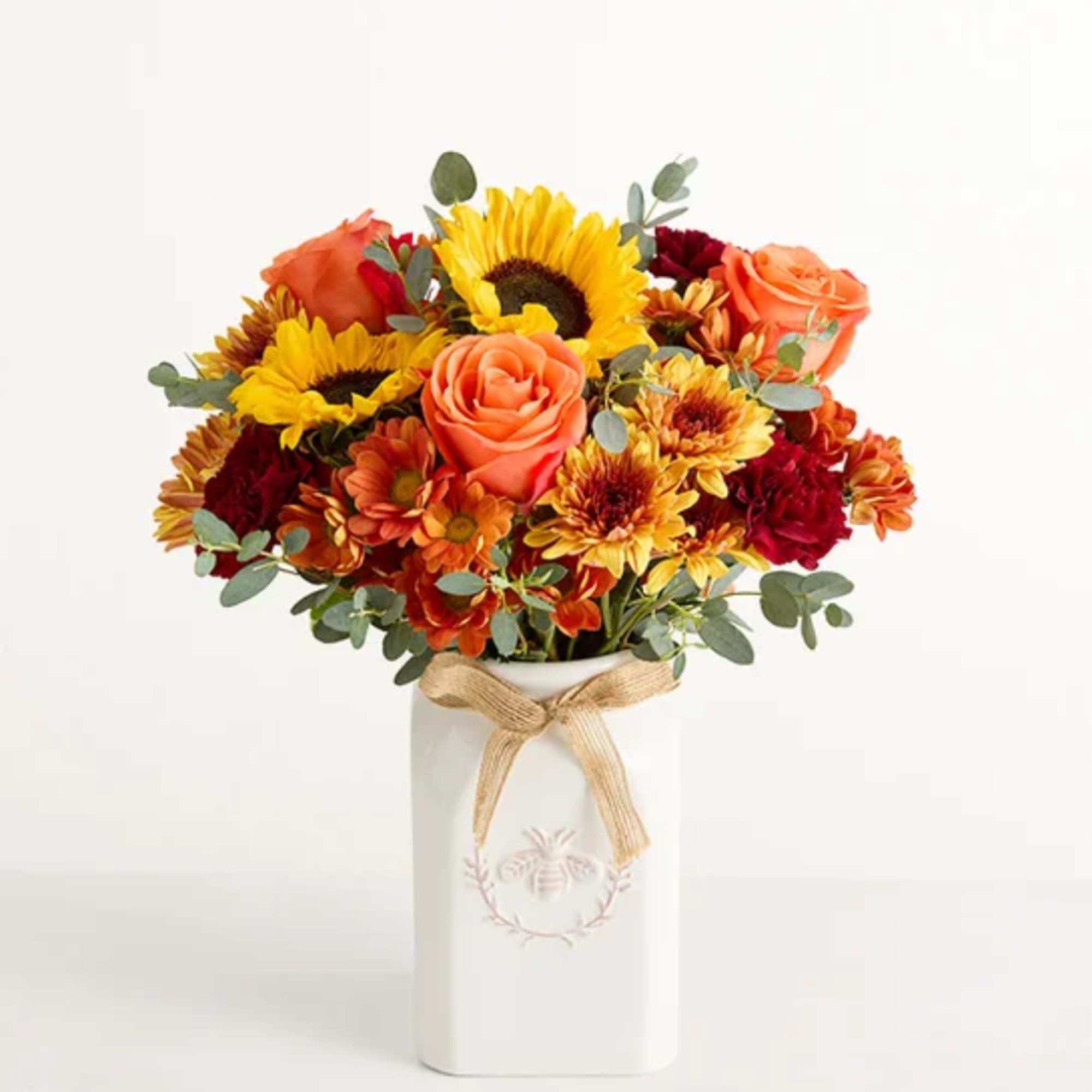 Bouquet of sunflowers, roses, and mums in a white vase with a ribbon