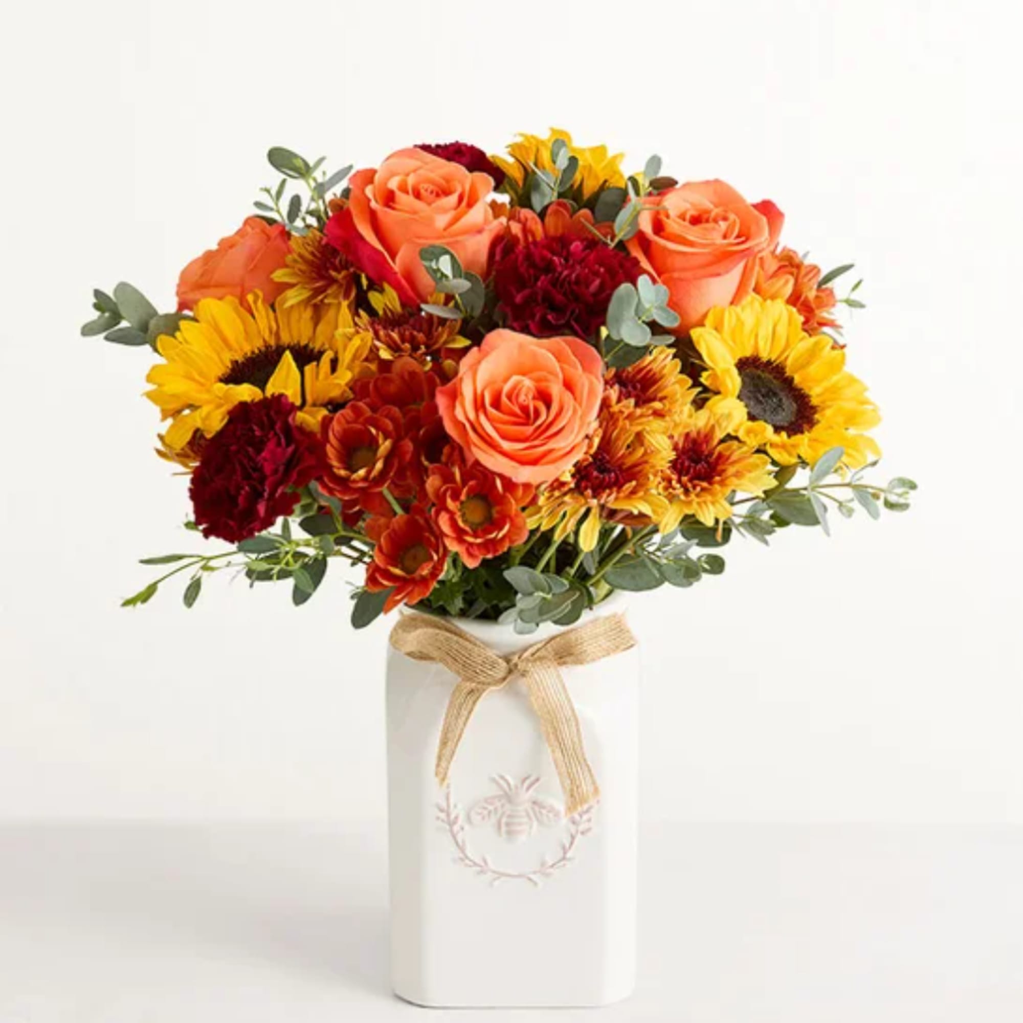 Bouquet of orange roses, sunflowers, and red mums in a white vase