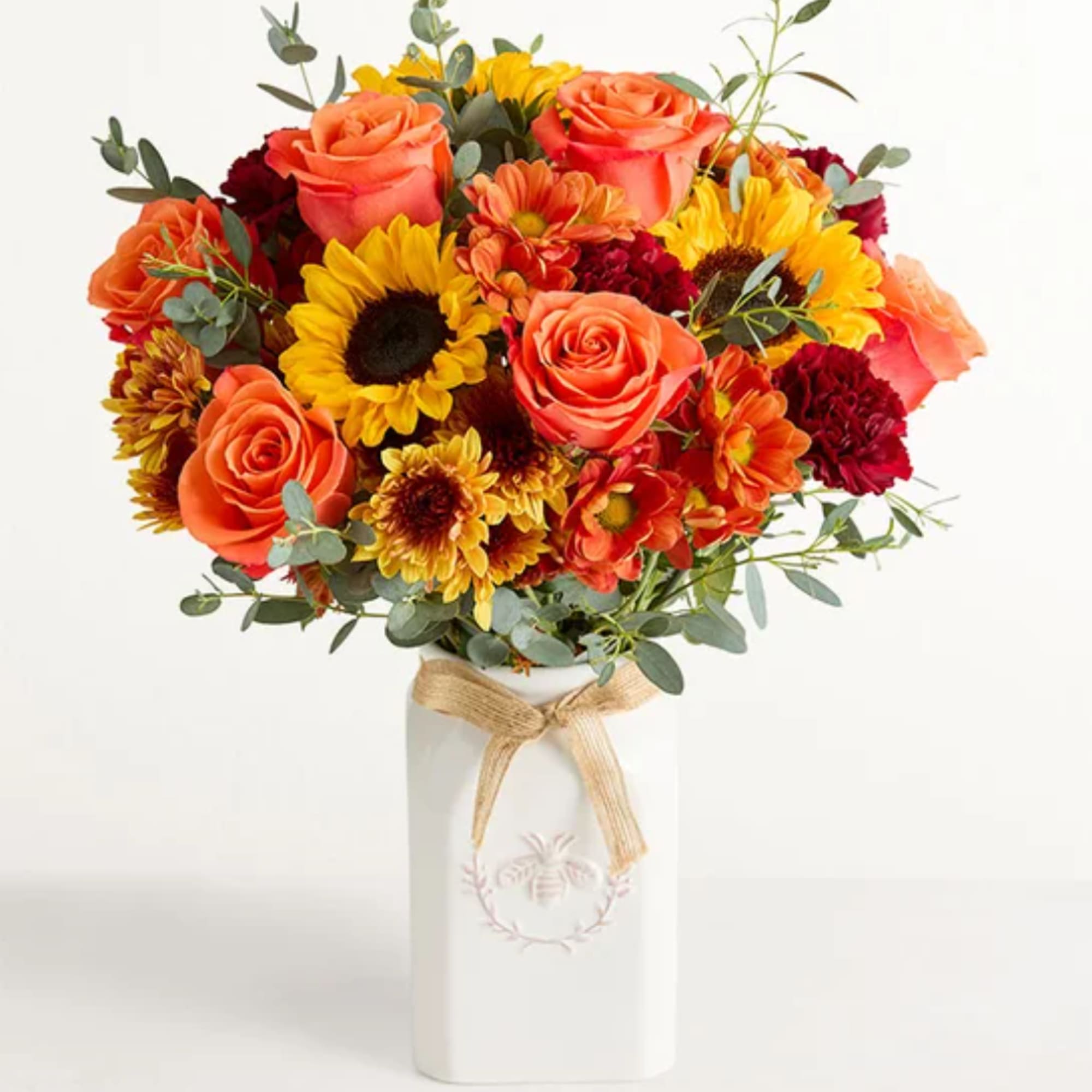 Orange roses and yellow sunflowers in a white vase with a ribbon