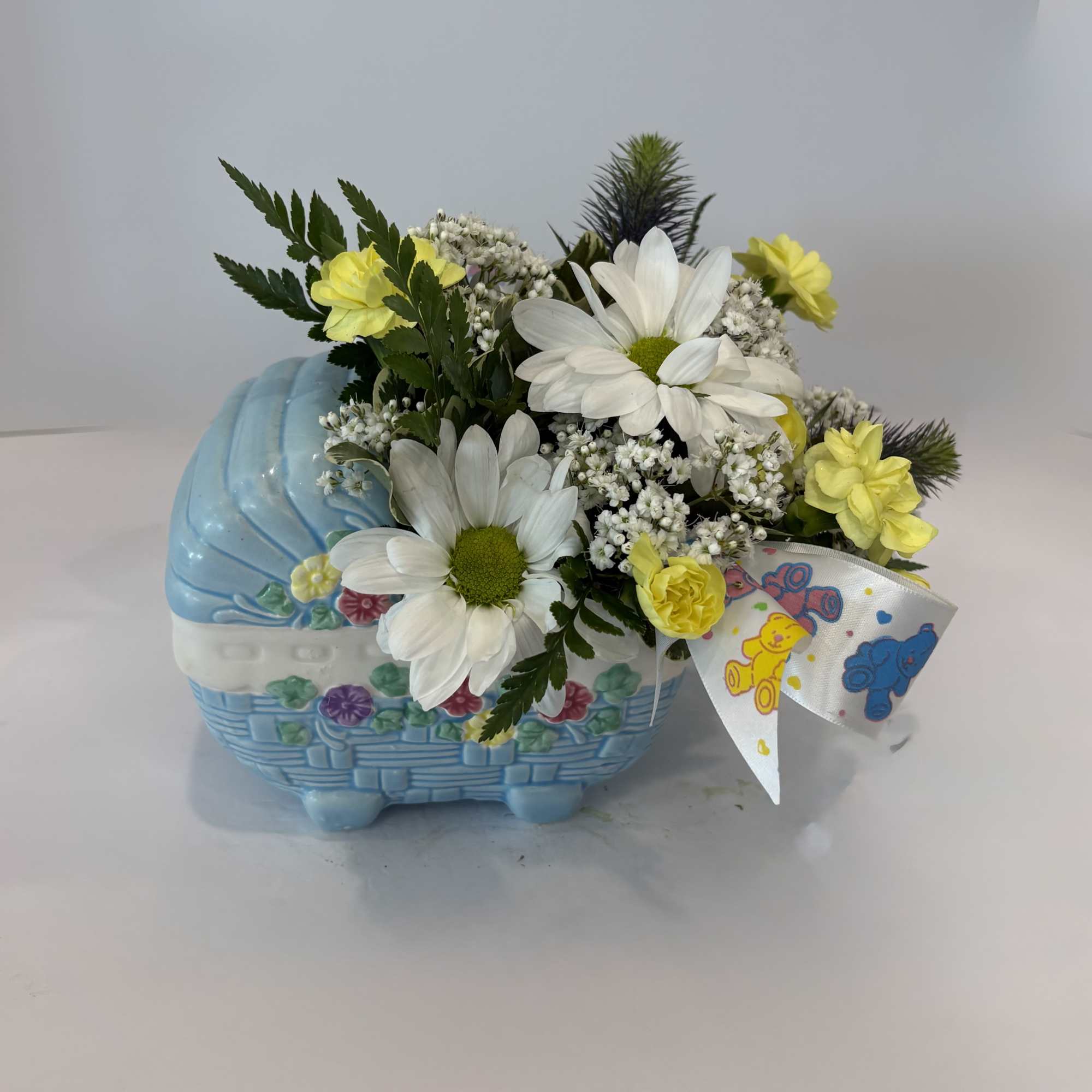 Yellow and white flowers arranged in a blue basket with a teddy bear ribbon