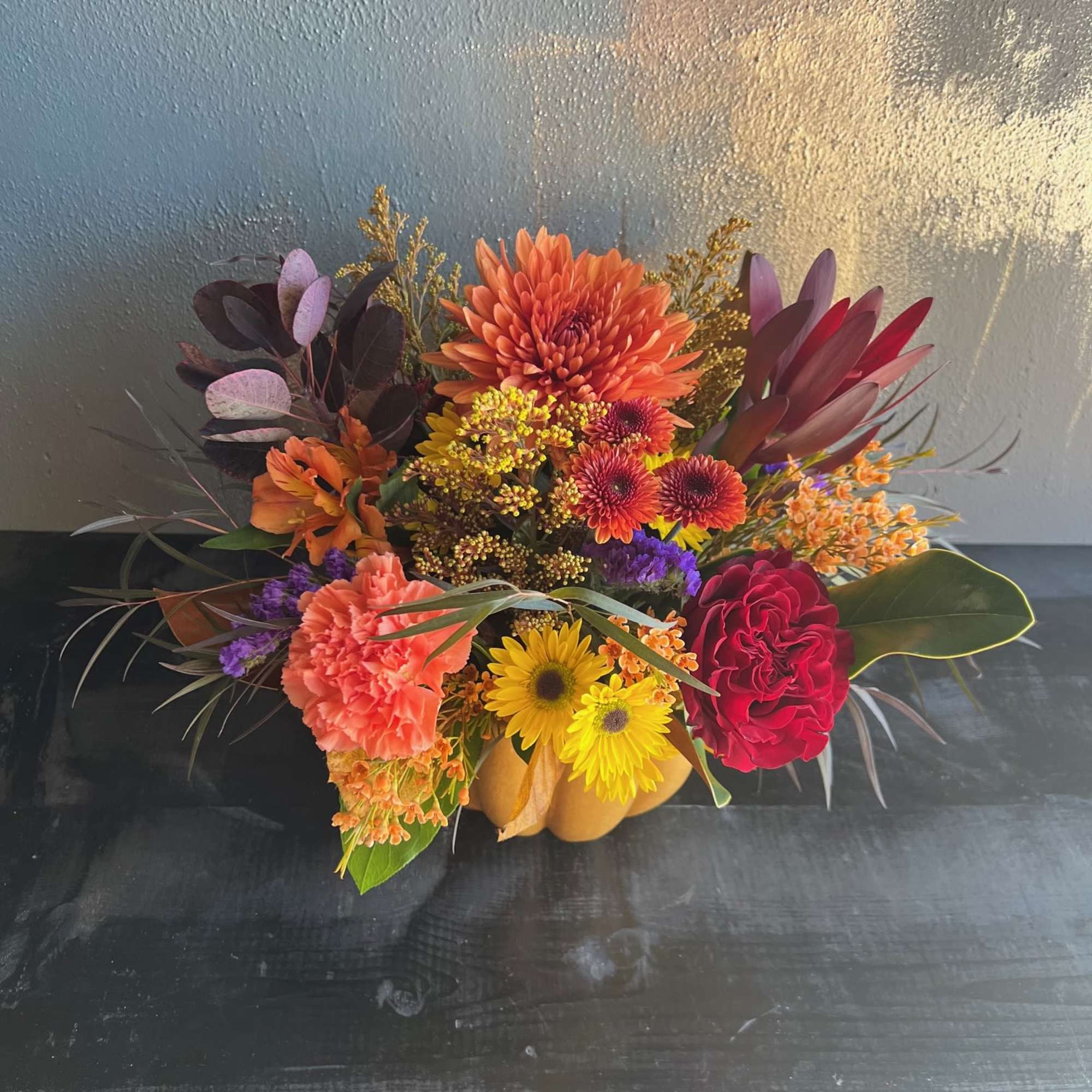 Autumn floral arrangement in a pumpkin-shaped container with orange, red, and yellow blooms