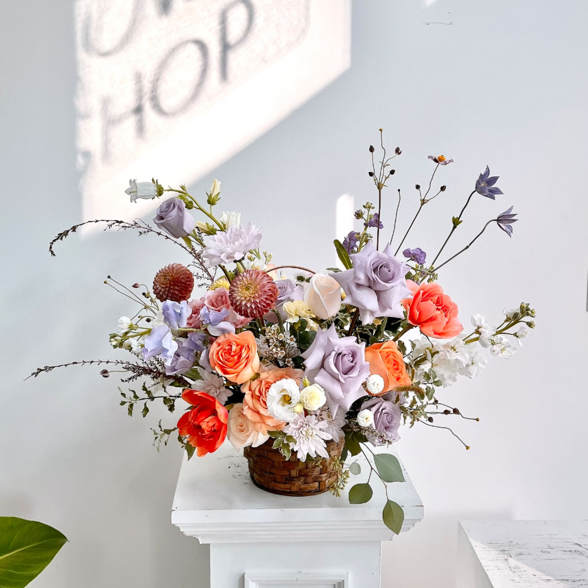 Mixed pastel floral arrangement in a woven basket on a white pedestal