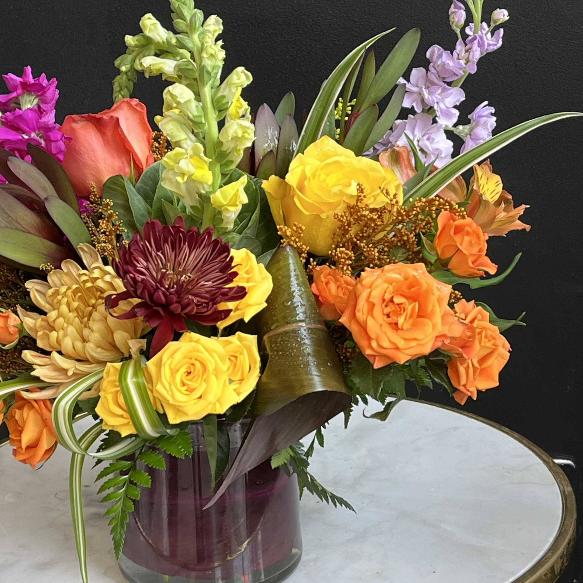 Colorful mixed bouquet in a glass vase with roses, chrysanthemums, and snapdragons