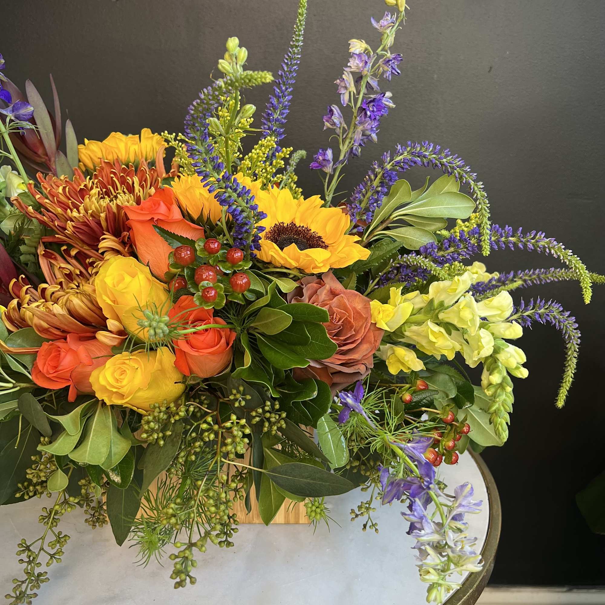 Colorful bouquet with sunflowers, roses, and purple spikes in a low vase