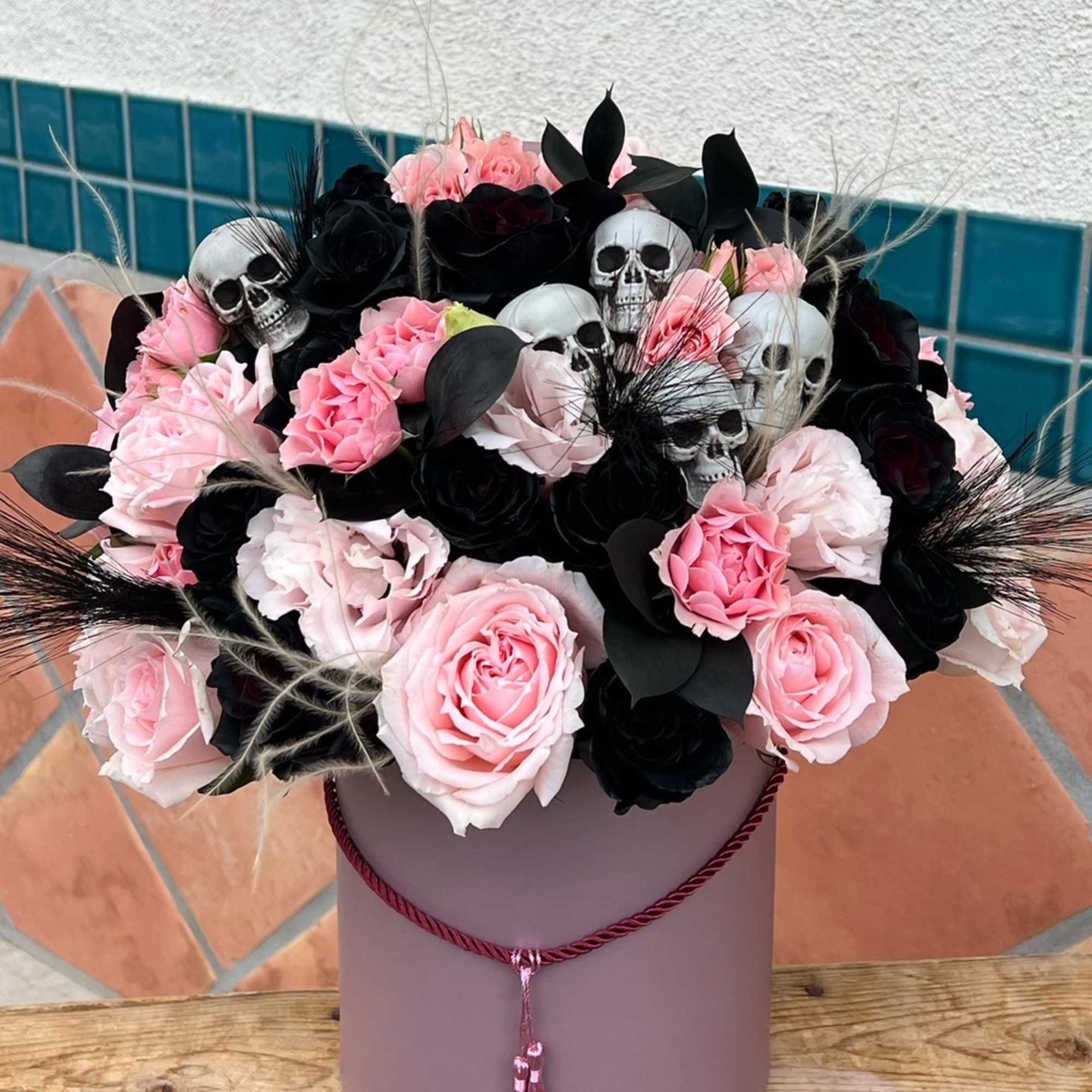 pink and black flowers arranged inside a pink flower box. 