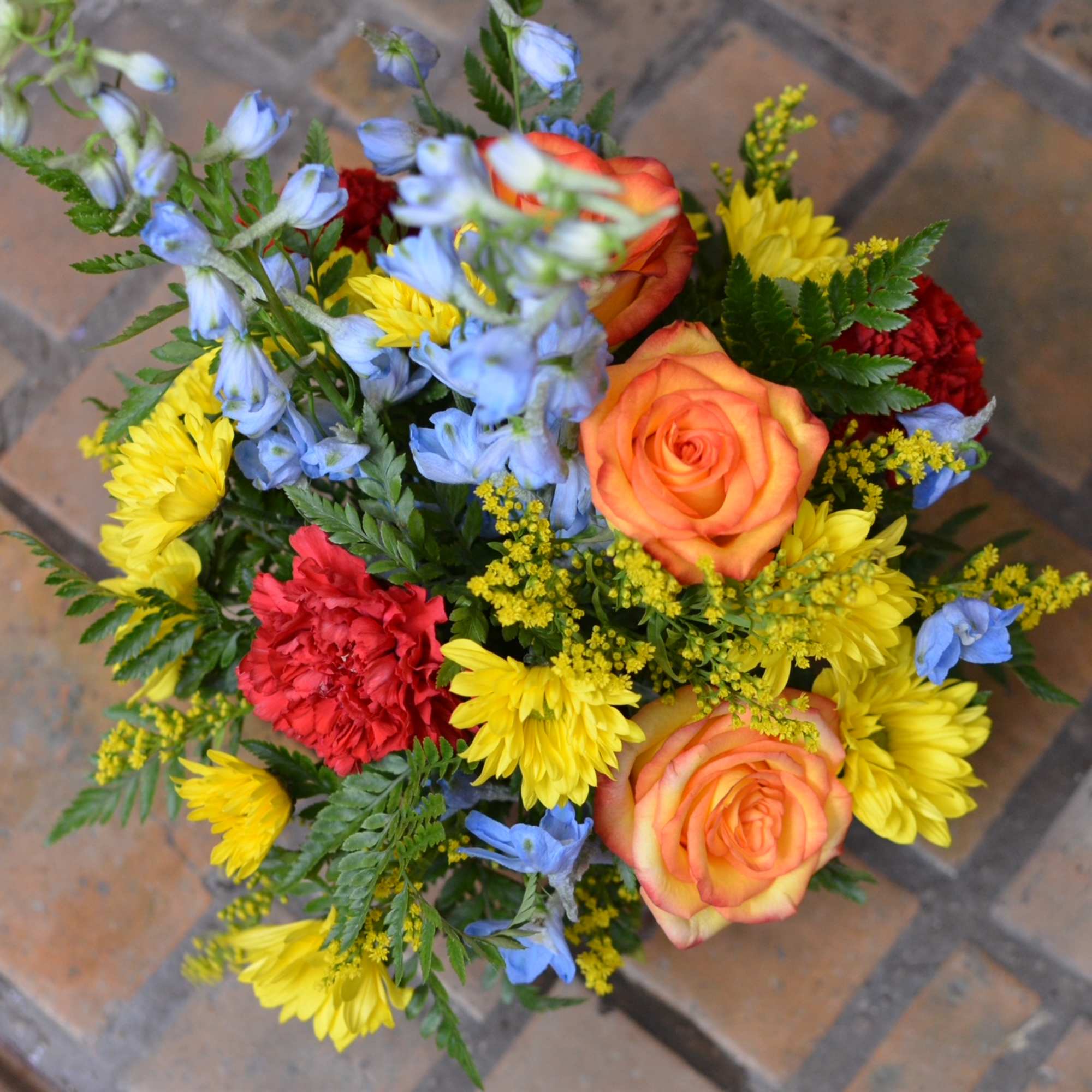 Colorful bouquet with orange roses, yellow daisies, and blue flowers