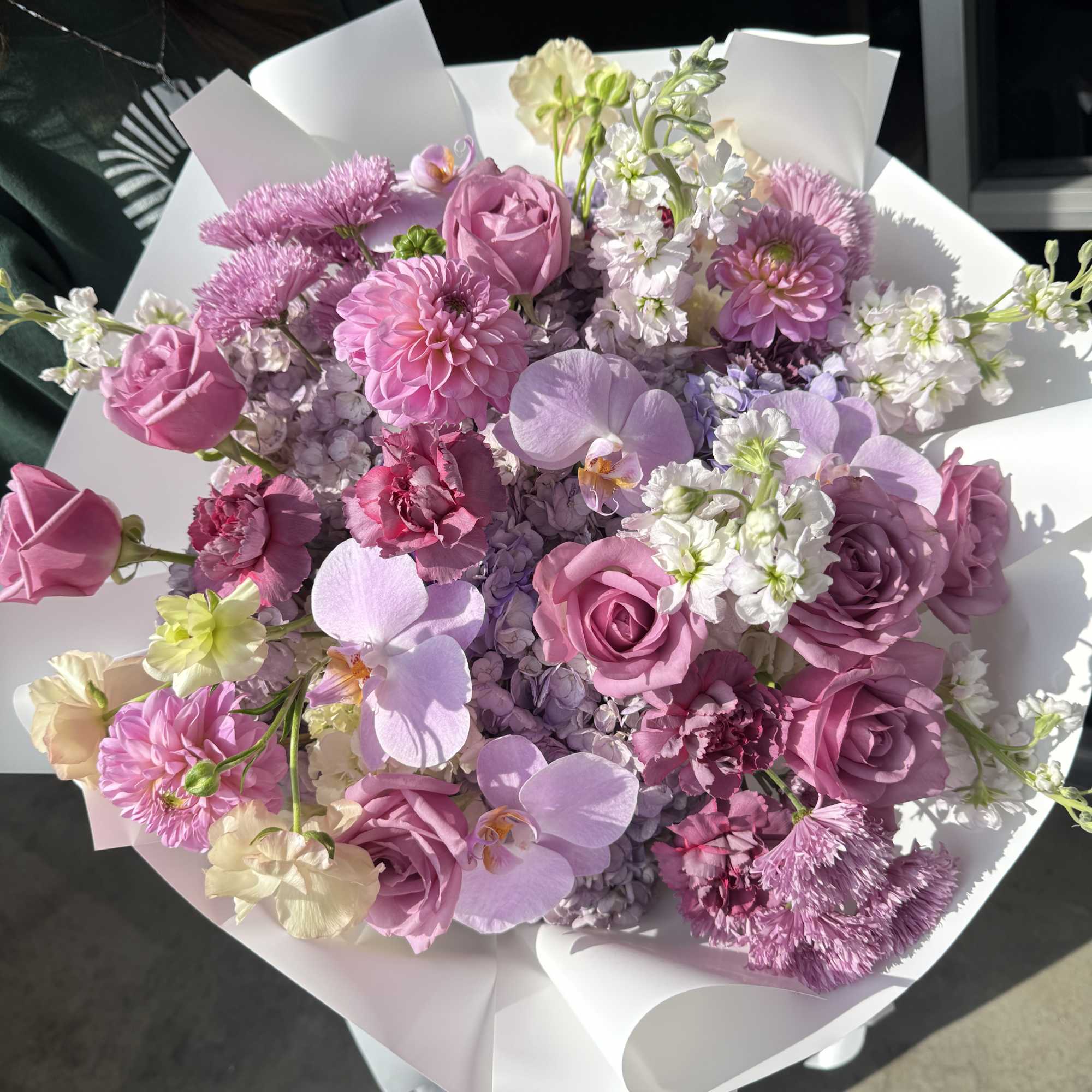 Pink and lavender bouquet with roses, orchids, and mixed blooms wrapped in white paper, photo 2 of 2