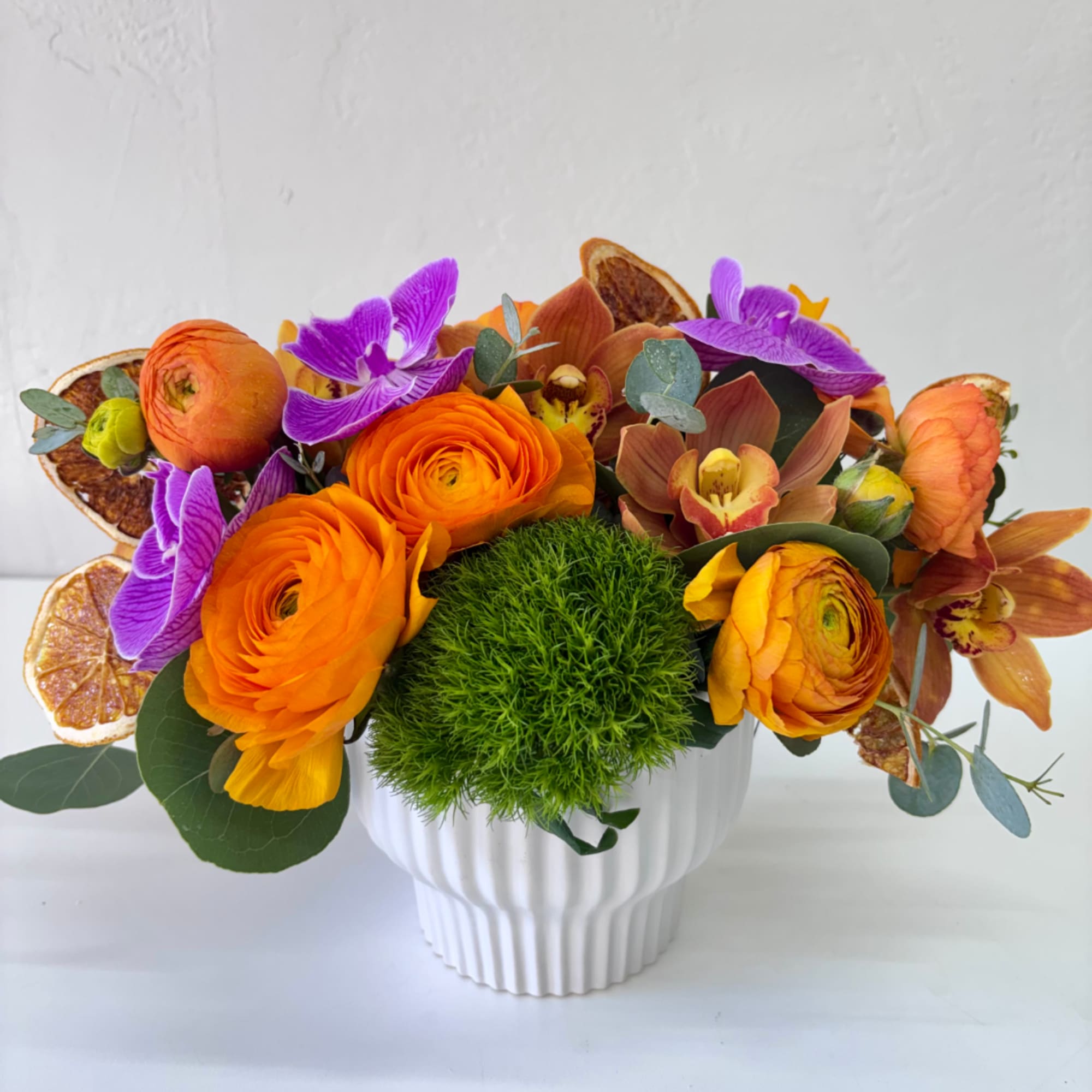 Orange and purple floral arrangement in a white ribbed vase