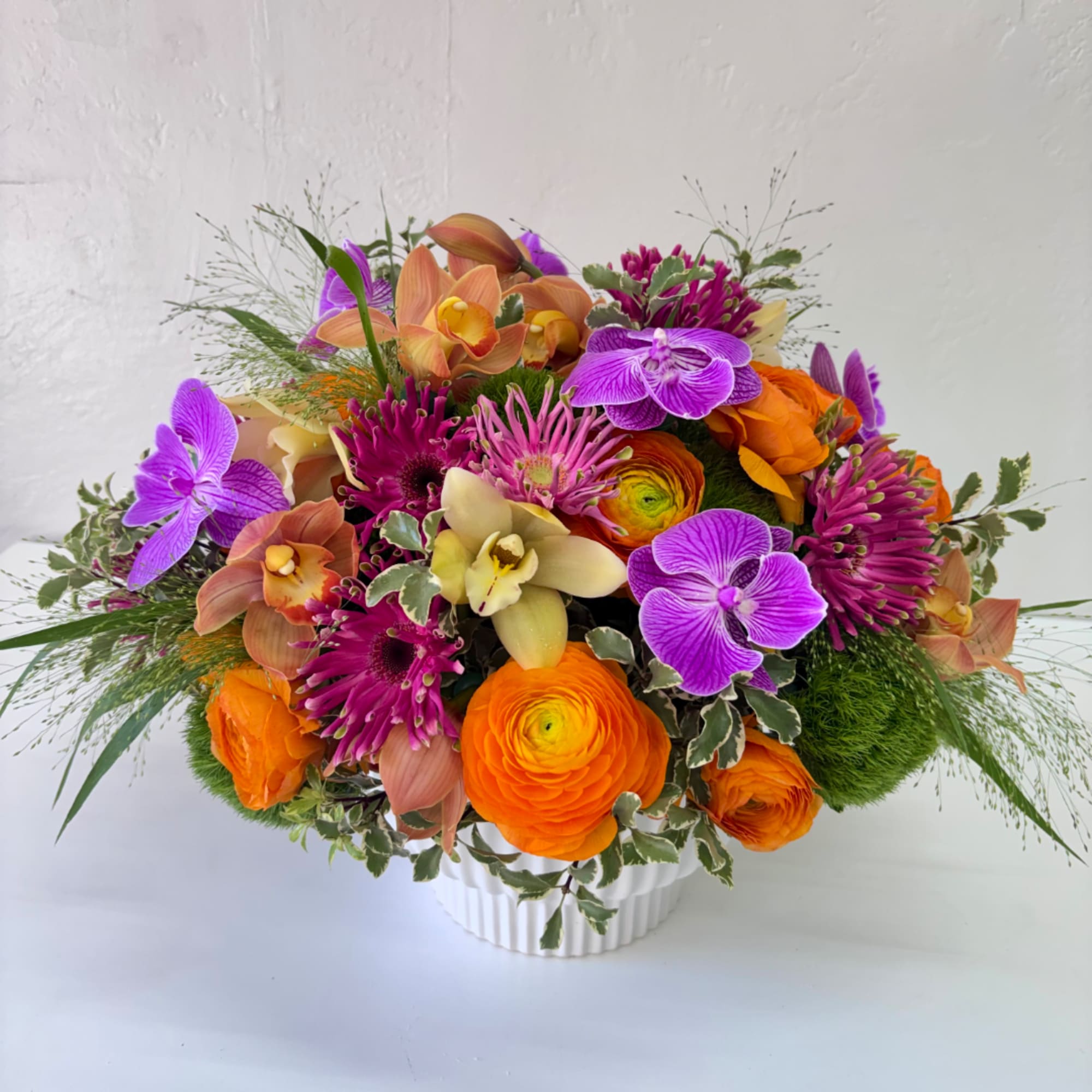 Bright mixed bouquet in a white vase with purple, orange, and peach blooms