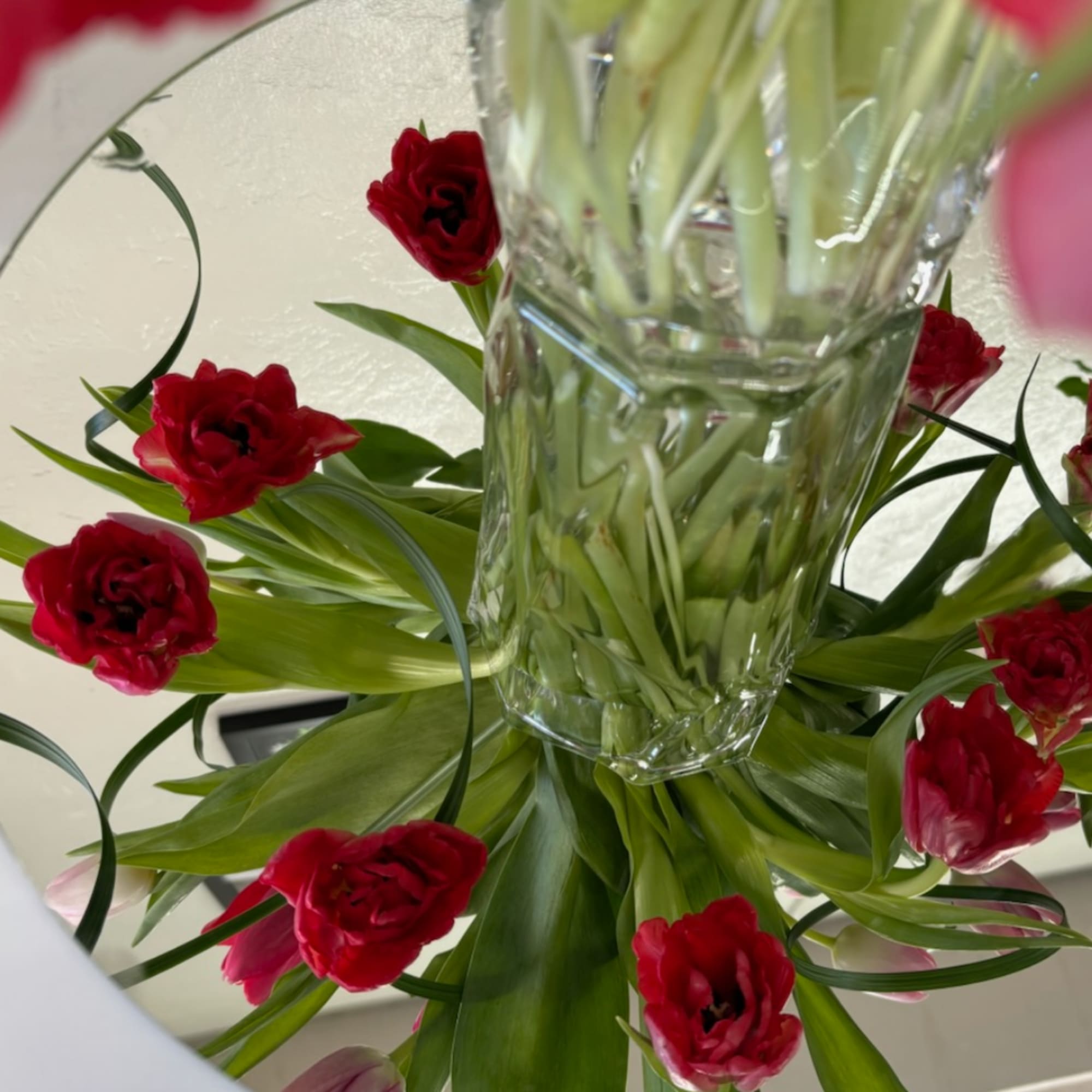 Red tulips arranged in a clear glass vase with broad green leaves