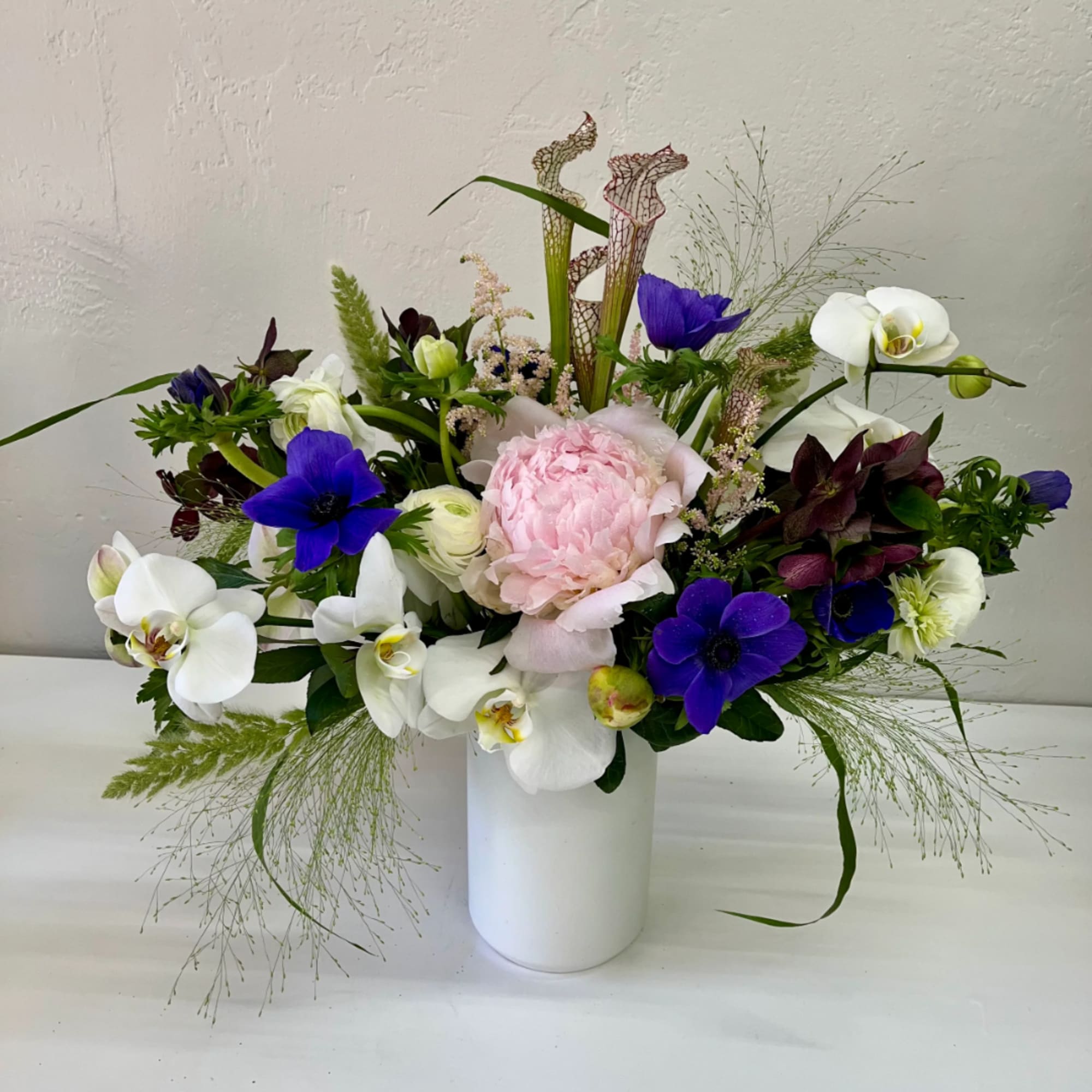 Mixed bouquet with pink peony, white orchids, and purple flowers in a white vase