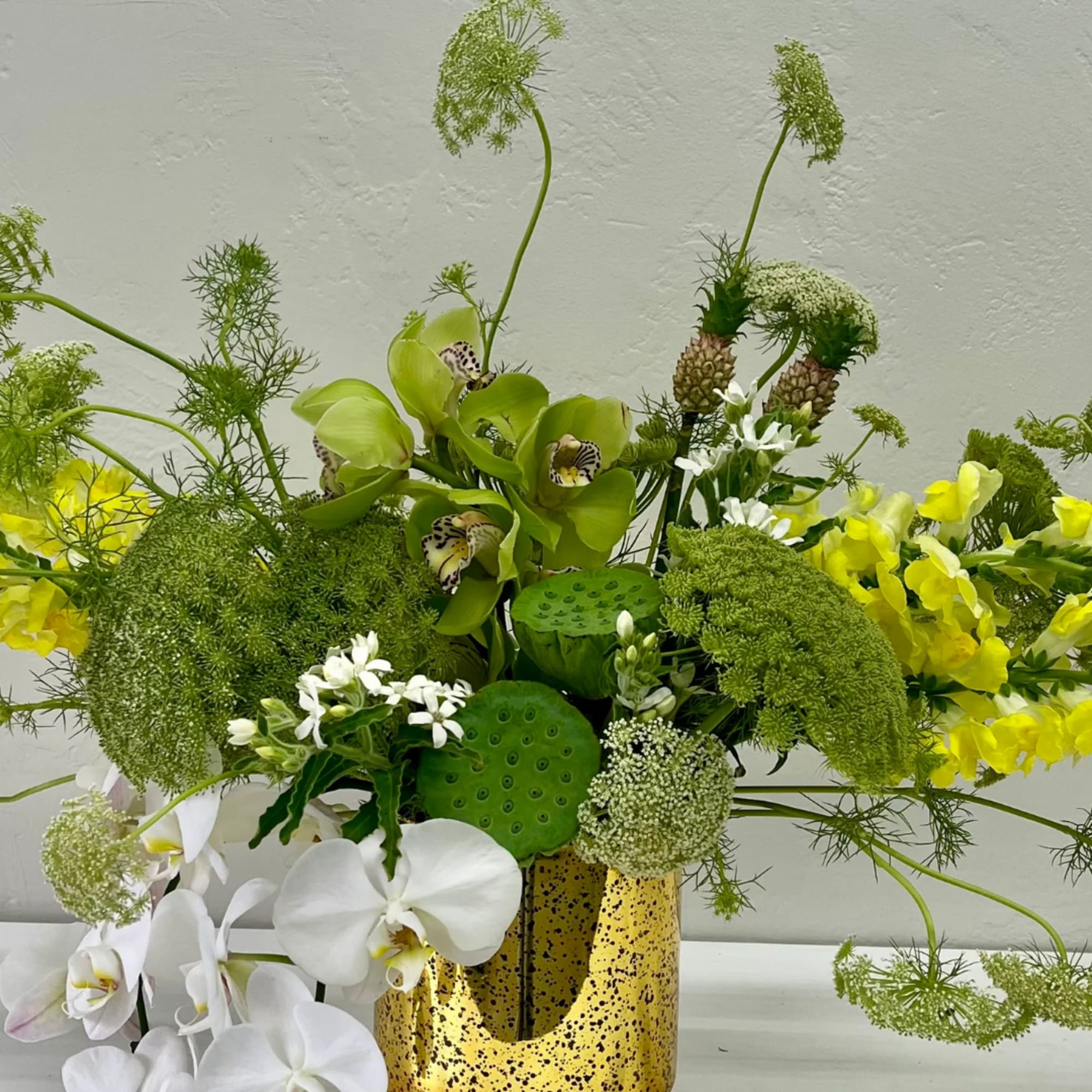 Green and white floral arrangement with orchids in a speckled gold vase