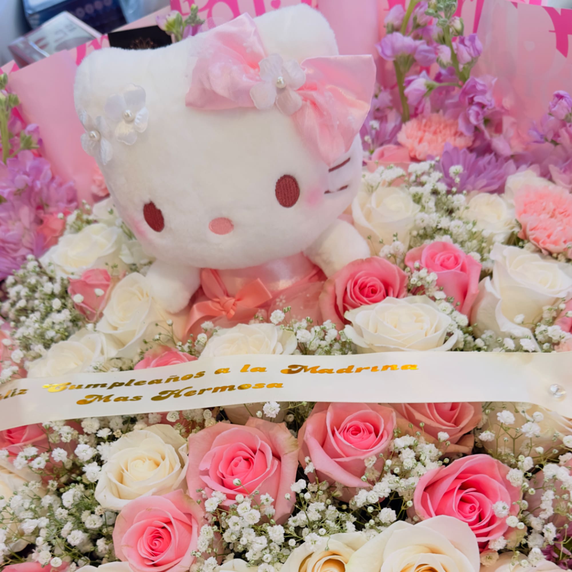 Hello Kitty plush surrounded by pink and white roses and baby's breath