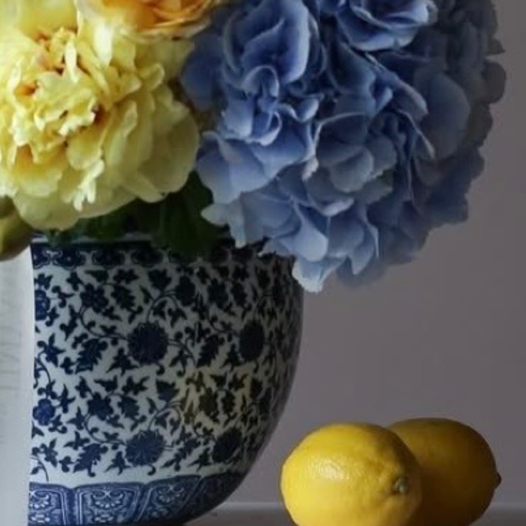 Blue and yellow hydrangeas in a patterned ceramic vase with two lemons nearby